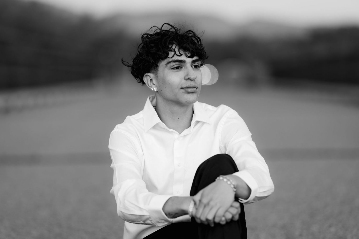 Black and white portrait of someone in white shirt sitting contemplatively outdoors.