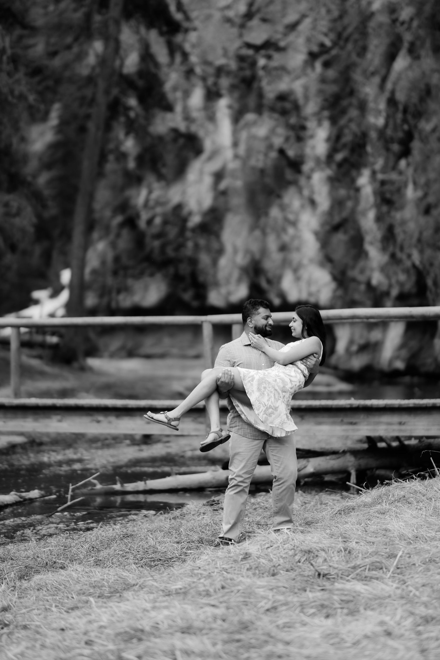 A romantic black and white moment captured outdoors as a couple embraces in a playful lift against a natural backdrop.