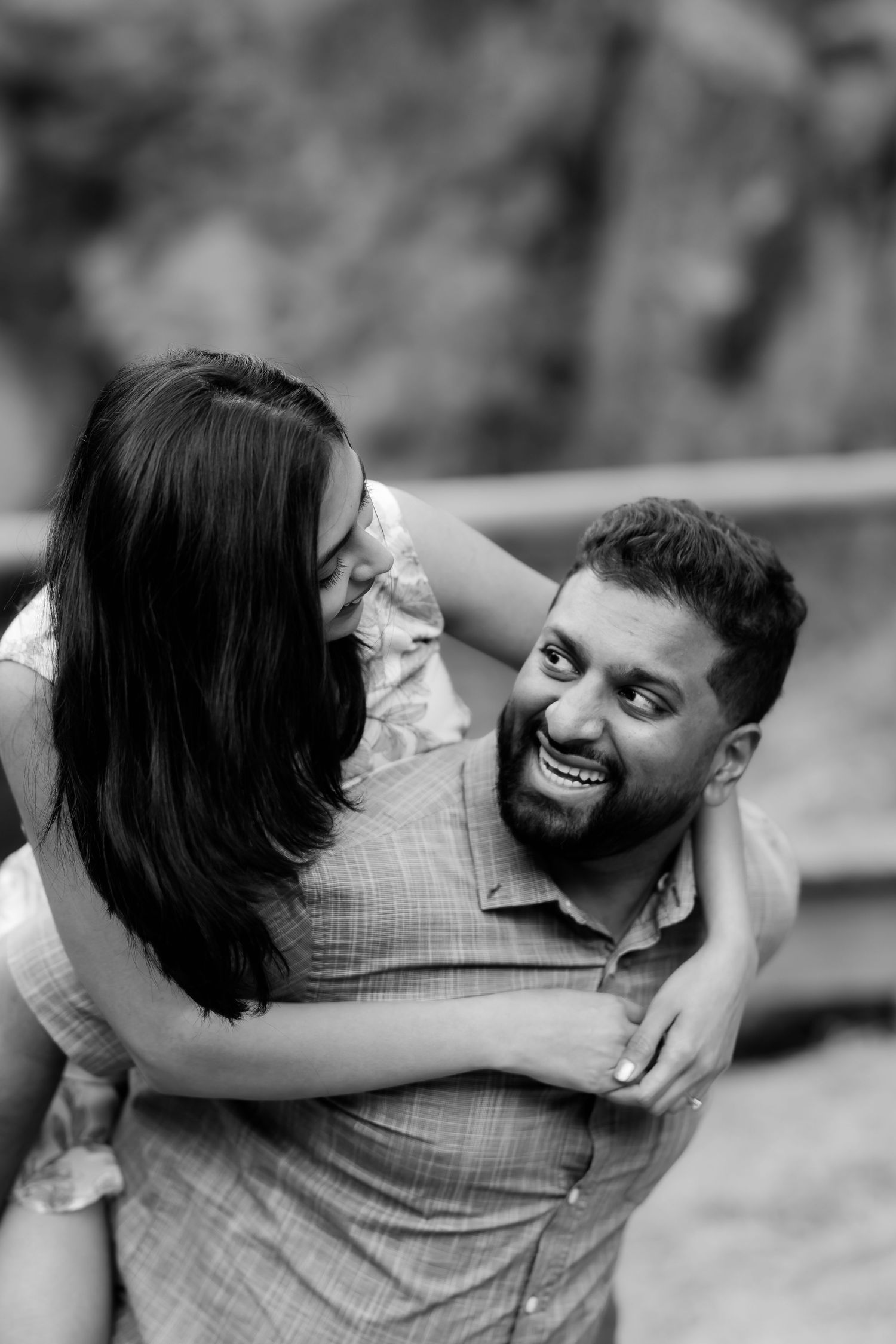 A joyful couple shares a playful black and white candid moment together outdoors.