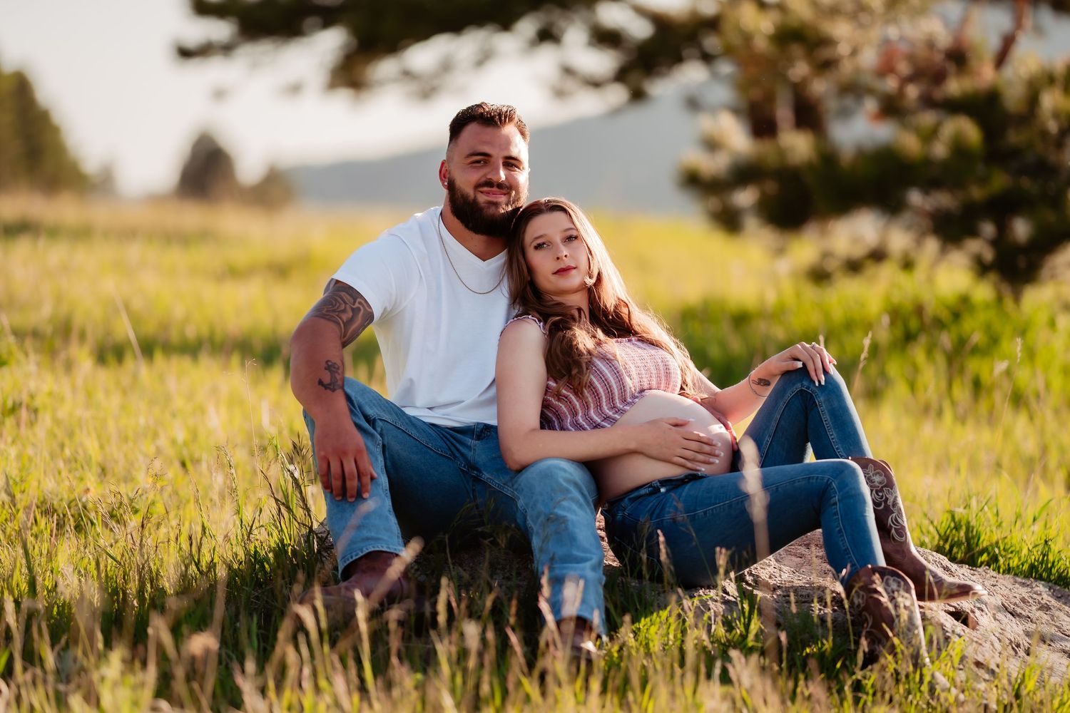 Two people relax together sitting on a rock in a sunny meadow with tall grass at sunset.