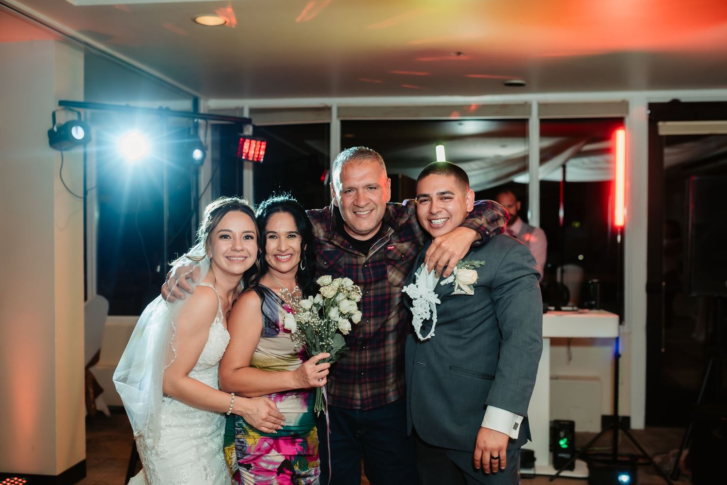 Wedding celebration with people dancing together at an indoor reception venue with colorful lighting effects.