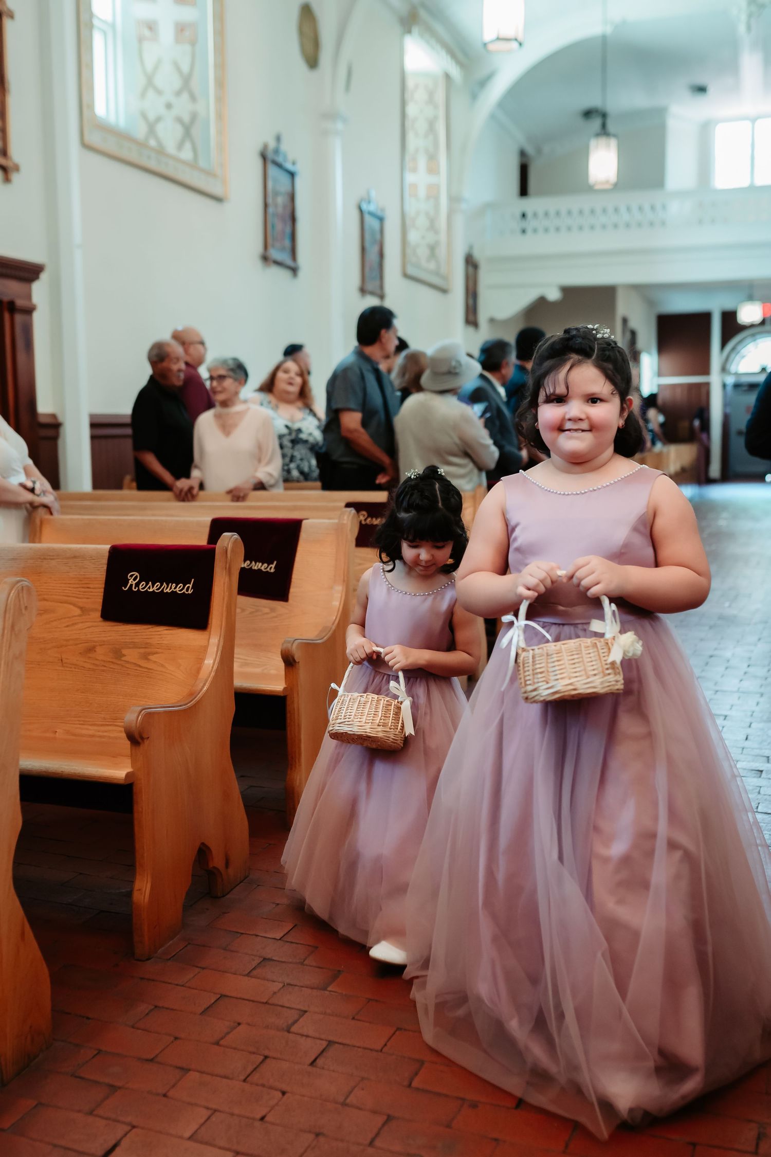 Bridesmaids in pink dresses wait in wooden church pews before the ceremony.