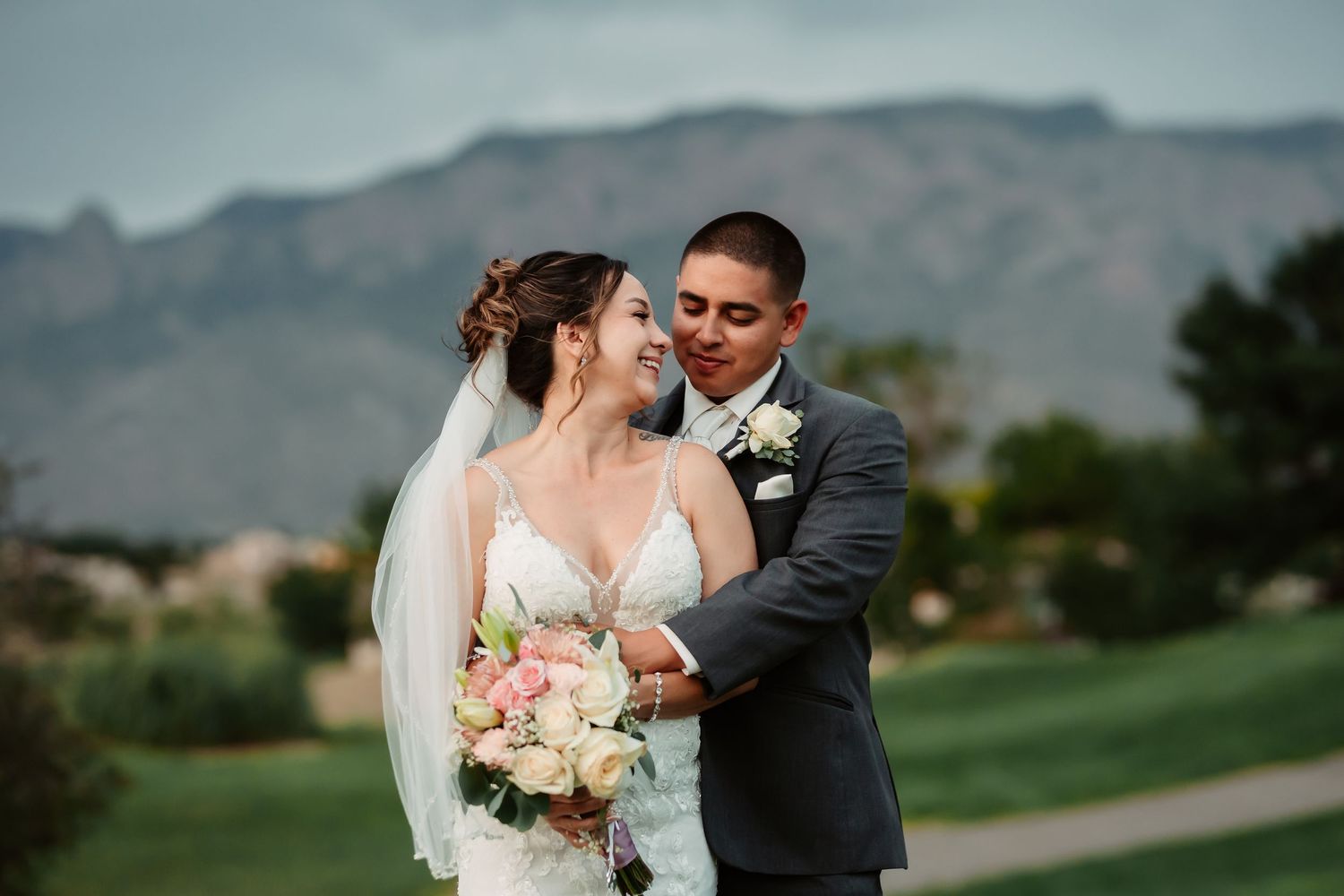 Newlyweds embracing outdoors with mountains and golf course scenery.