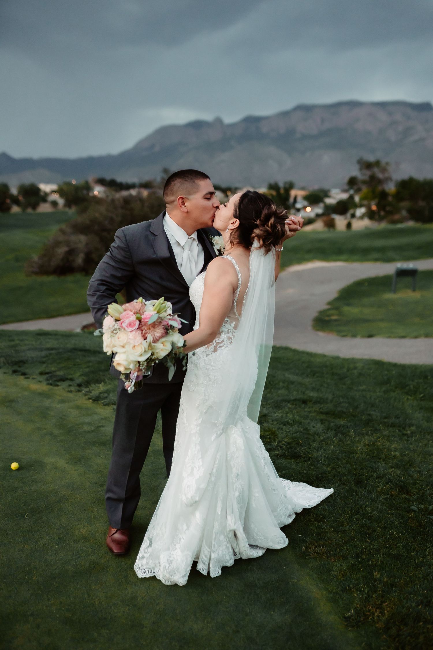 Wedding couple dances on a scenic golf course with mountain backdrop at sunset.