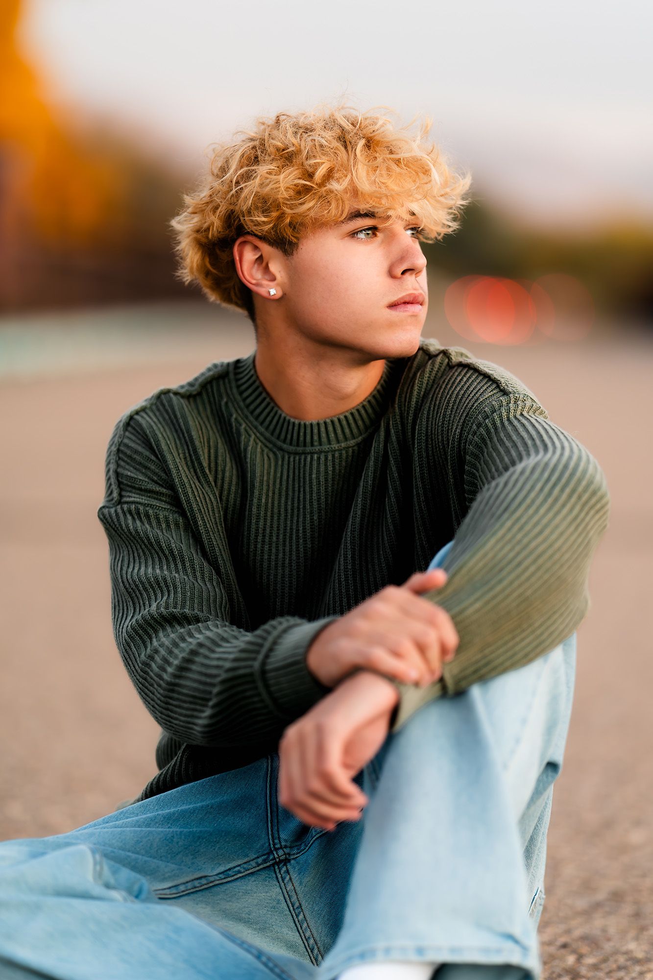 Portrait of person in green sweater and light jeans sitting outdoors during golden hour.