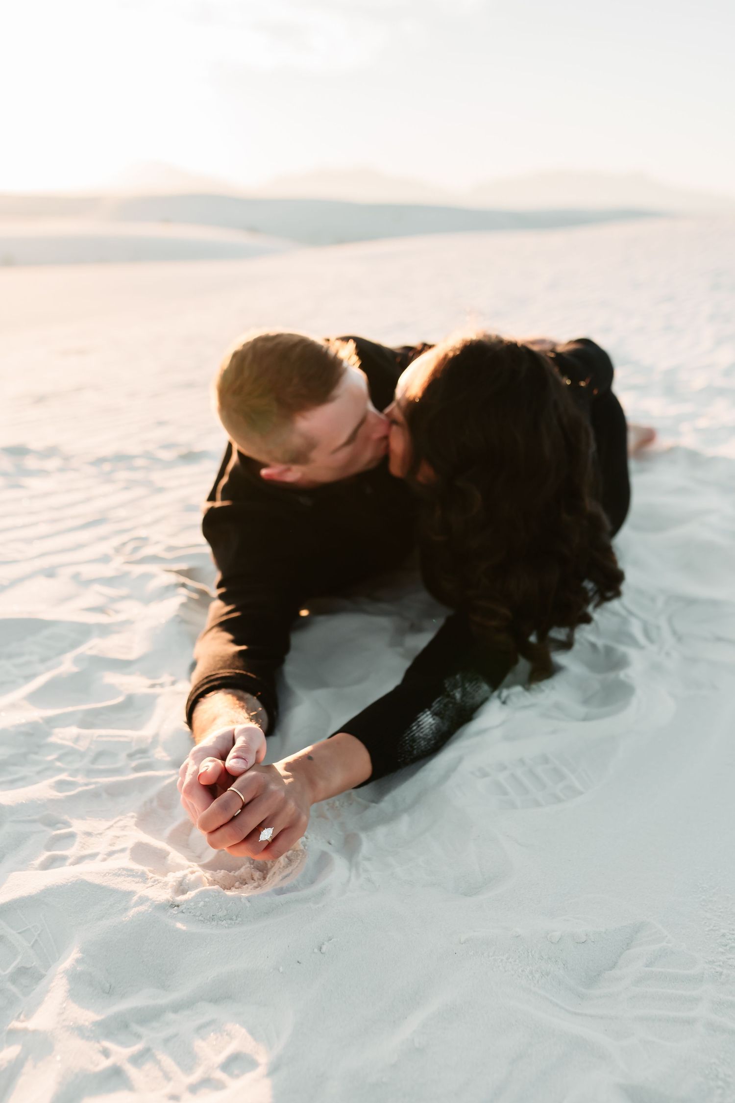 A couple embraces intimately while lying in pristine white snow during a romantic winter photoshoot.