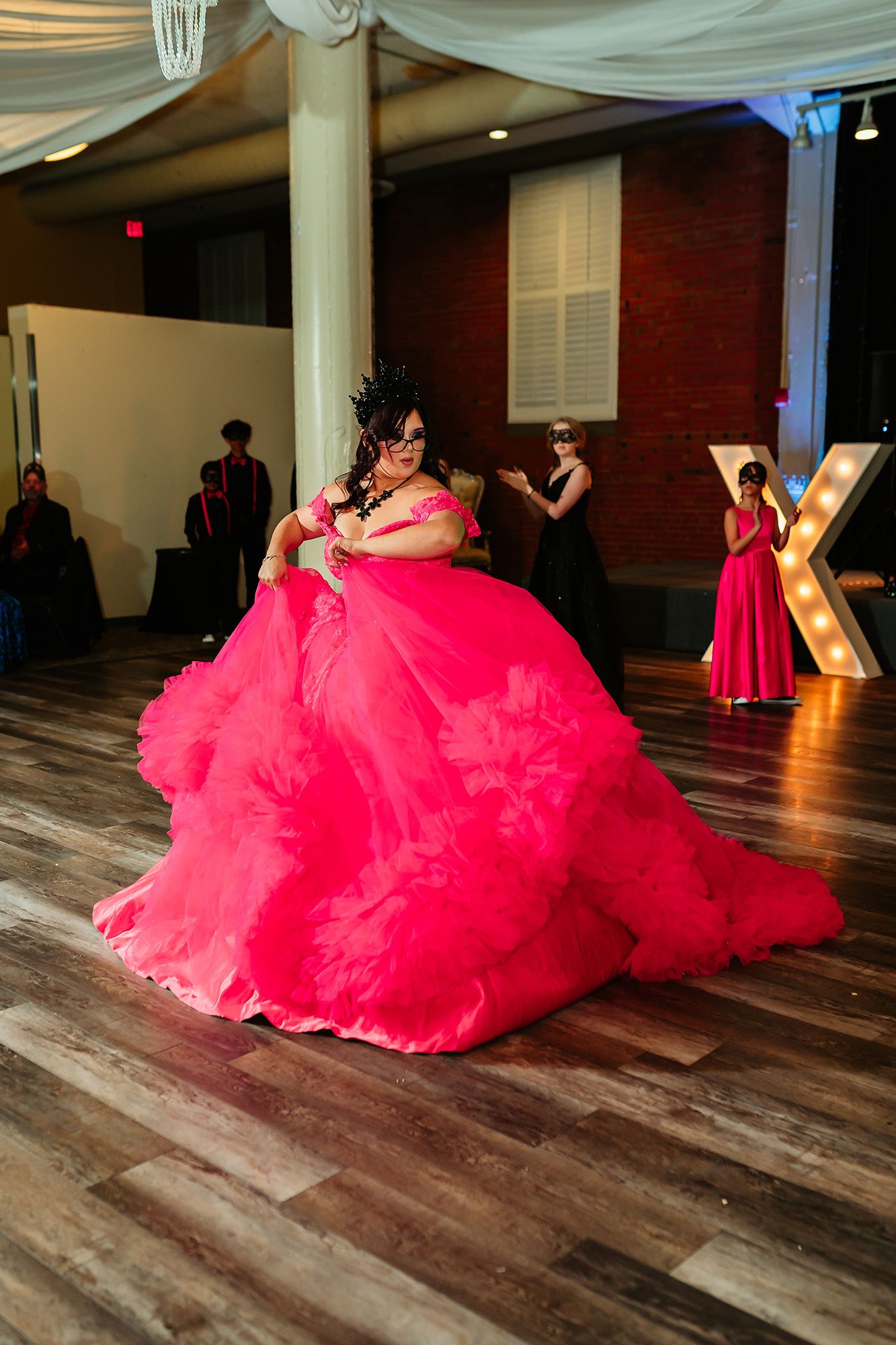A person in a flowing hot pink ballgown poses dramatically on a wooden floor during a photoshoot session.