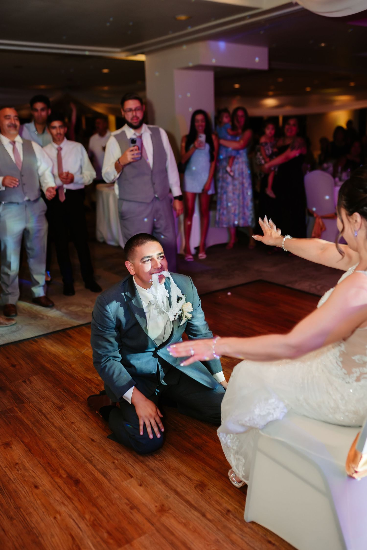 Wedding couple performs a dip dance move on hardwood floor while guests watch and take photos.