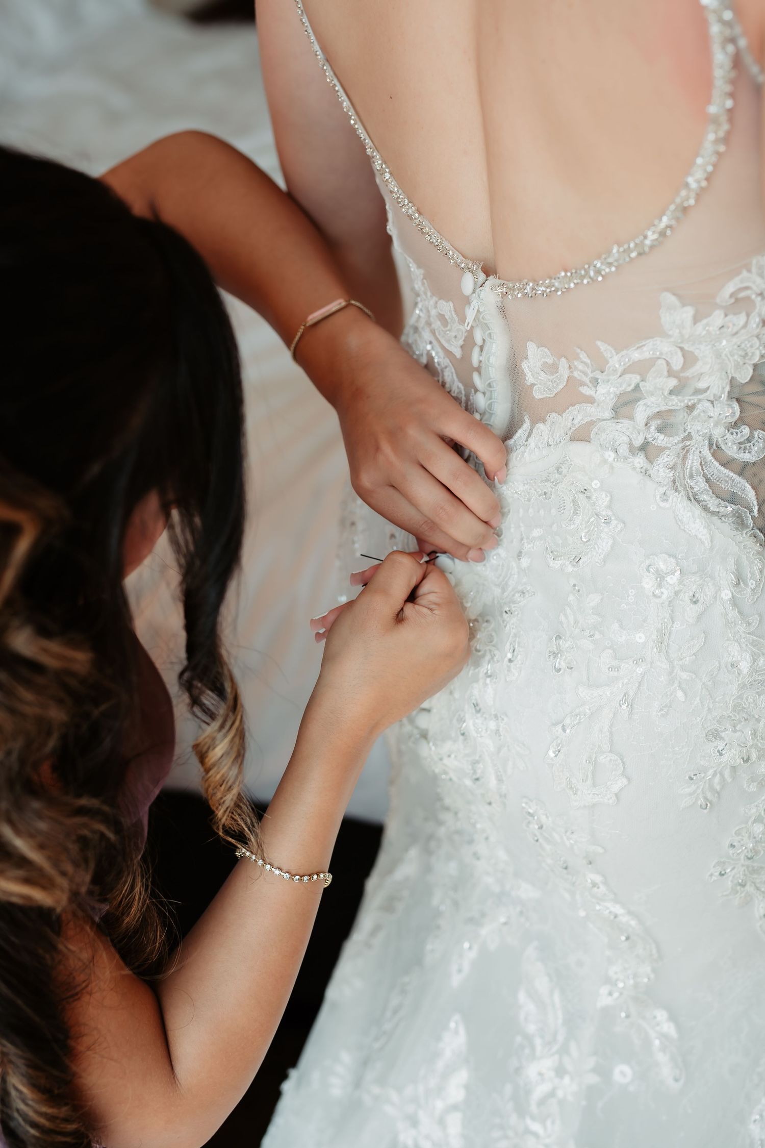Hands carefully fasten the back buttons and details of an ornate white wedding gown.