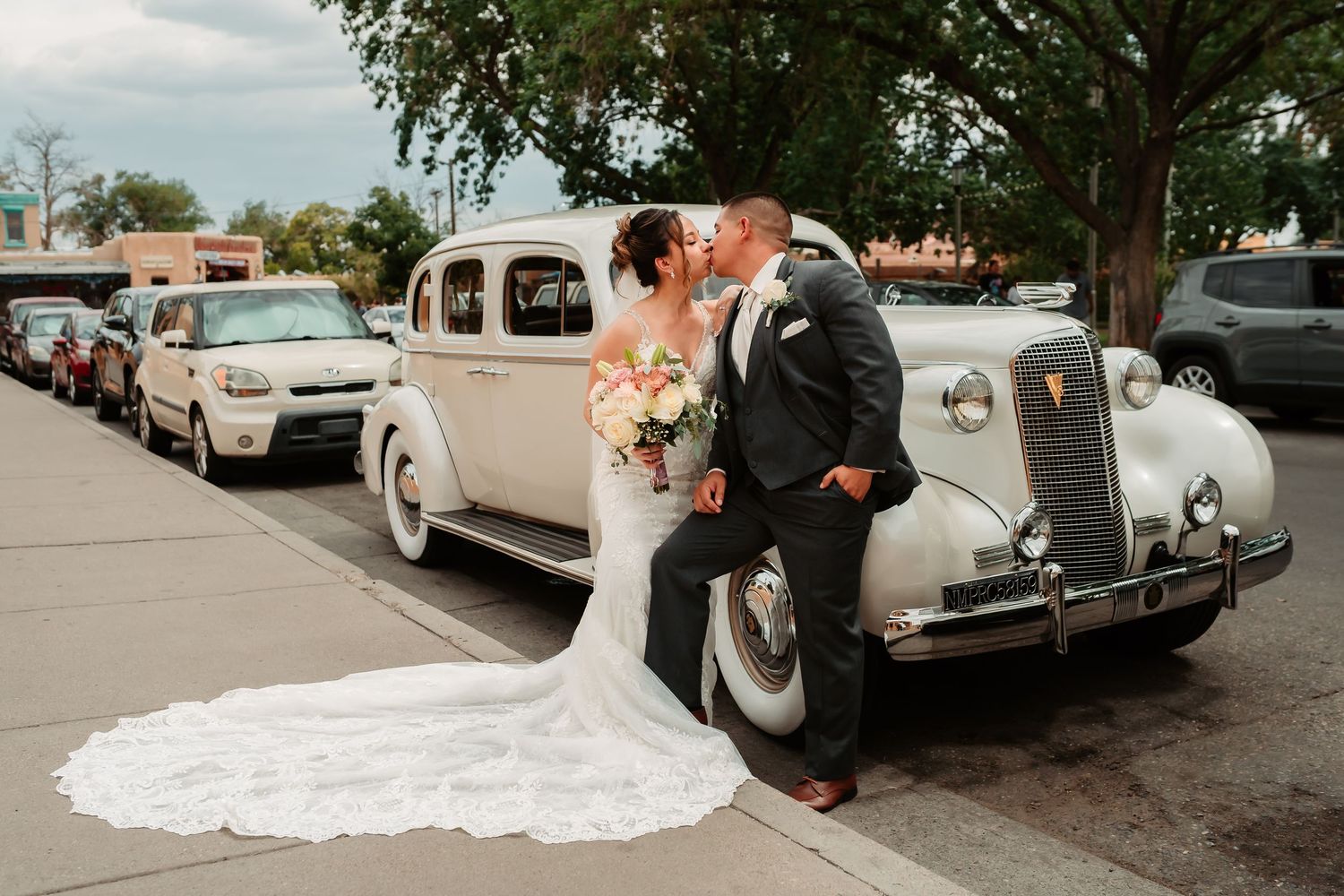 A vintage cream-colored classic car functions as a wedding getaway vehicle decorated with flower ornaments.