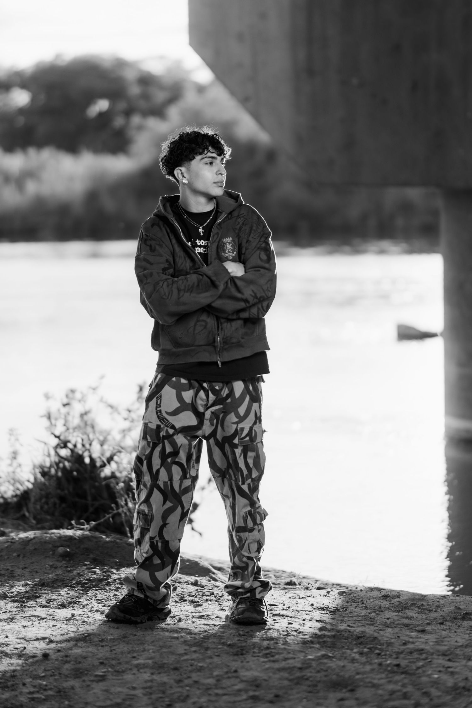 Black and white portrait of someone in casual wear with patterned pants standing outdoors.