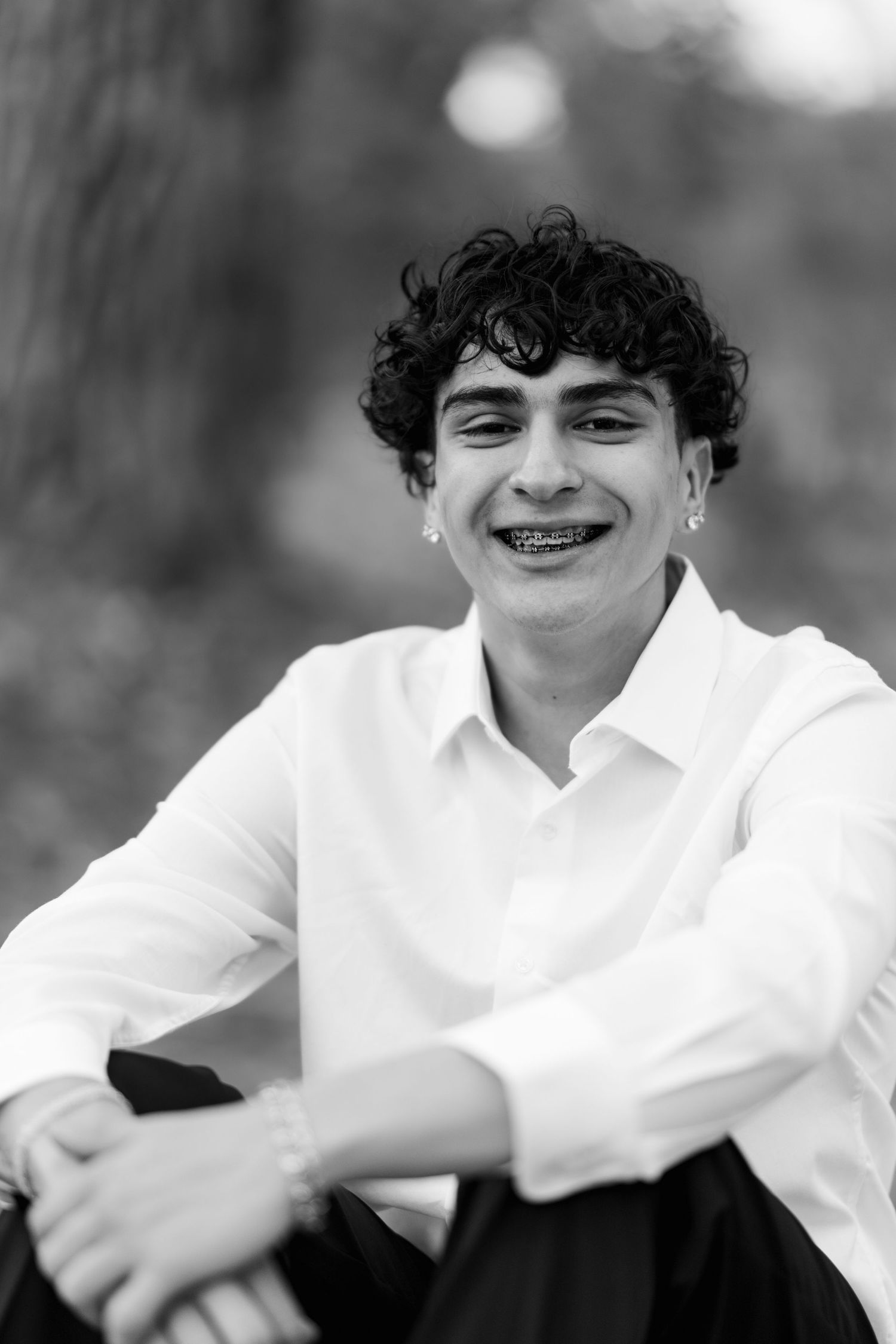 A black and white portrait of a person in a white button-up shirt smiling warmly at the camera with curly hair.