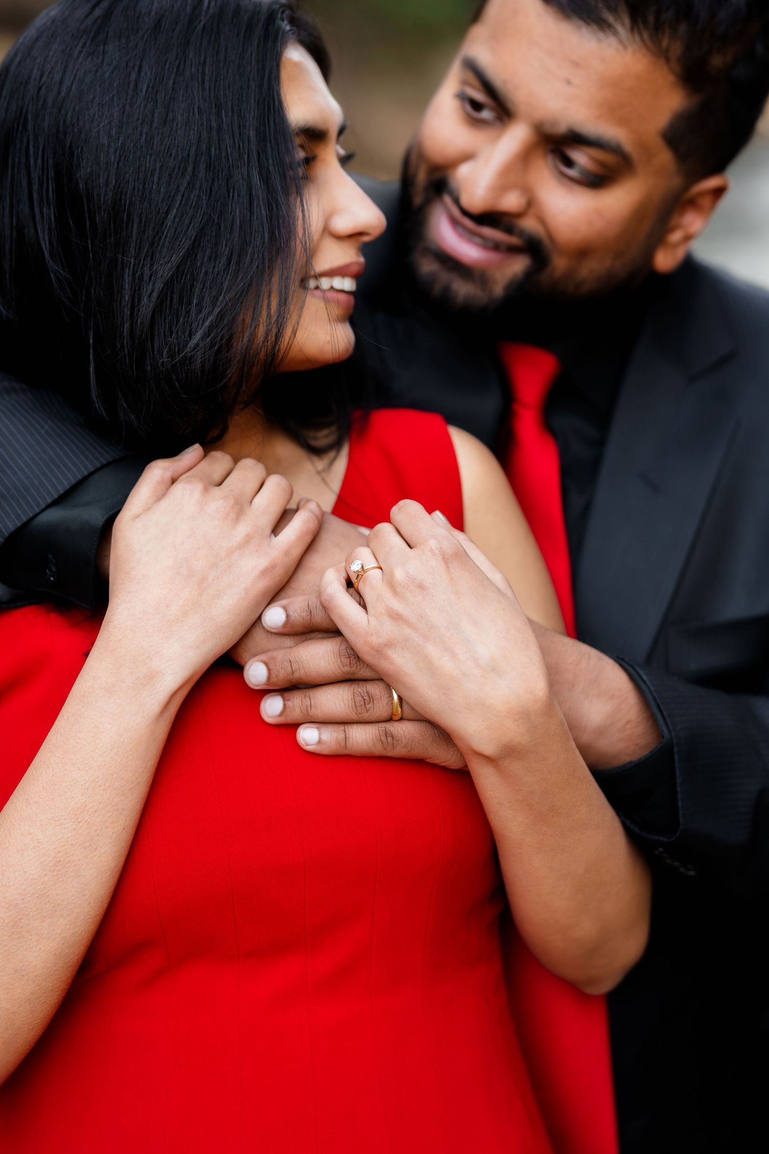Romantic couple embraces tenderly with woman in red dress as partner holds her from behind.