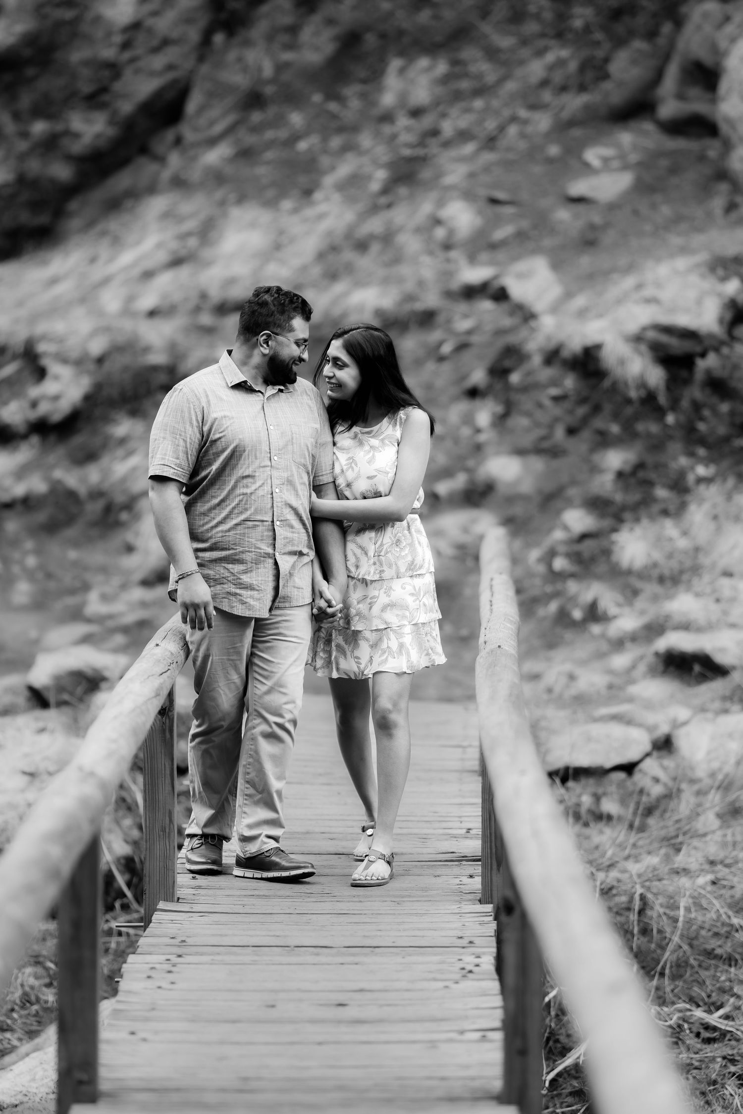 A couple shares an intimate moment while standing on a wooden boardwalk with scenic cliffs behind them.