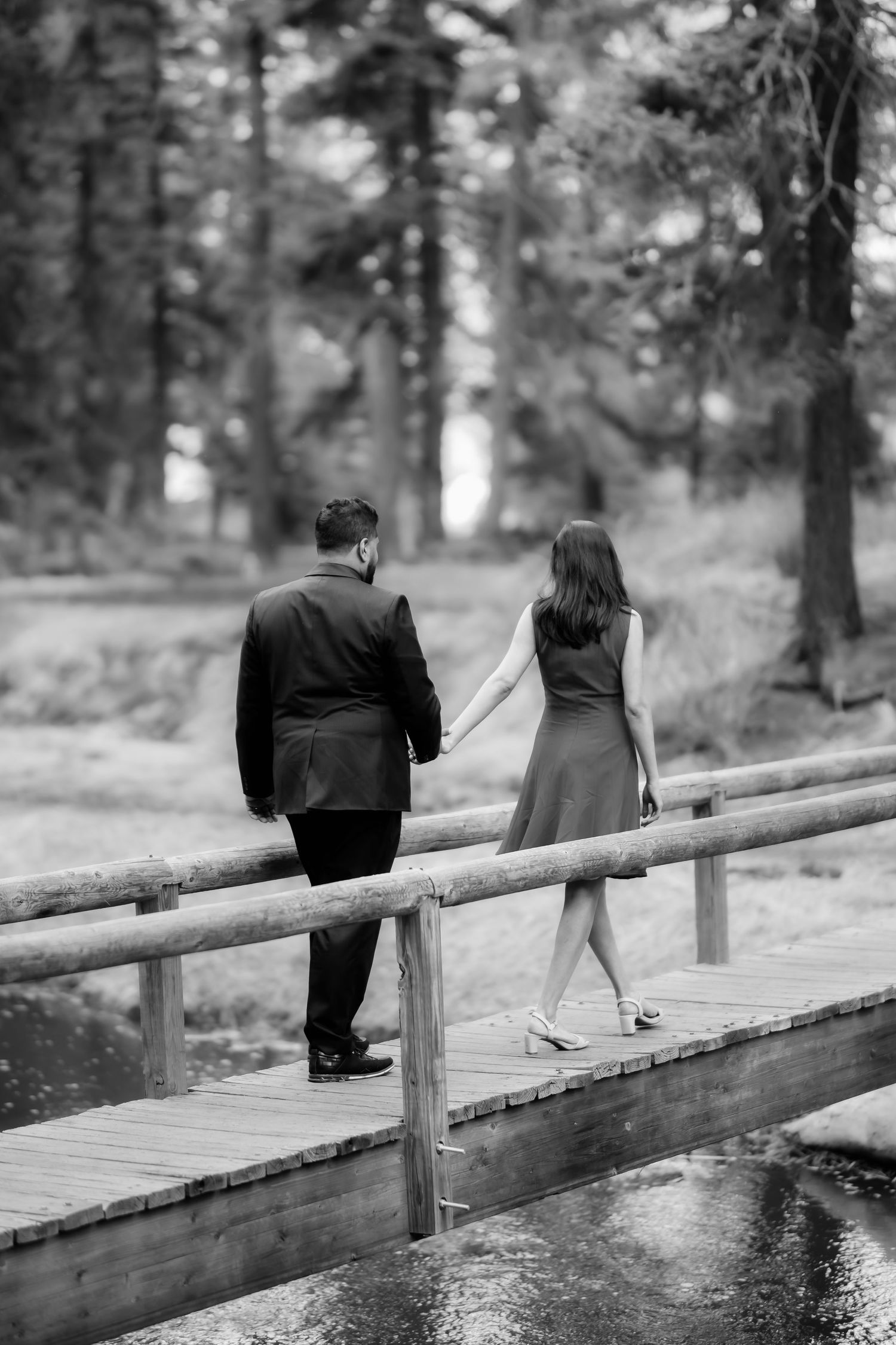 A couple walks together on a wooden footbridge through a serene forest setting.