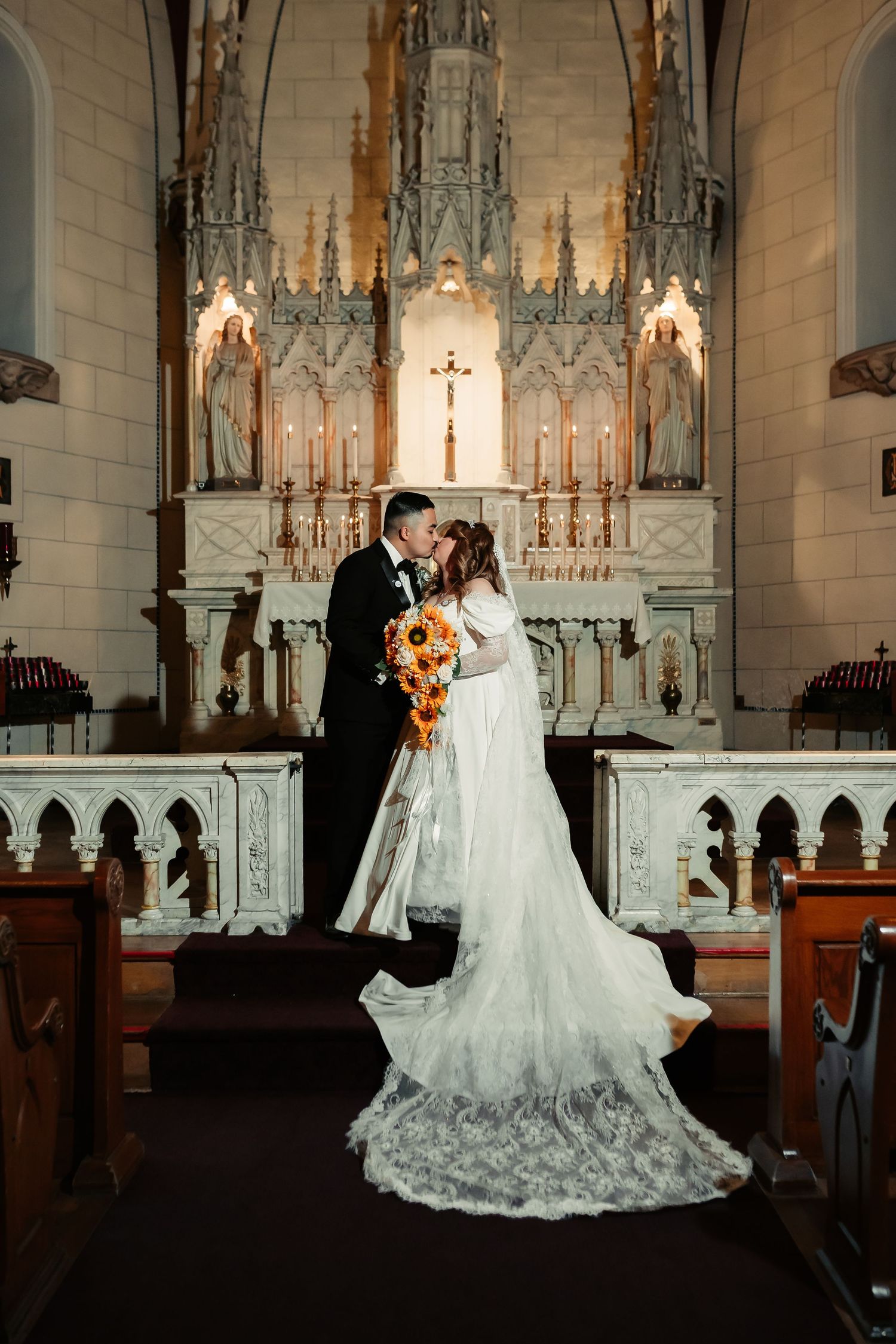 A couple shares their first kiss during a traditional Catholic church wedding ceremony with ornate gothic architecture.