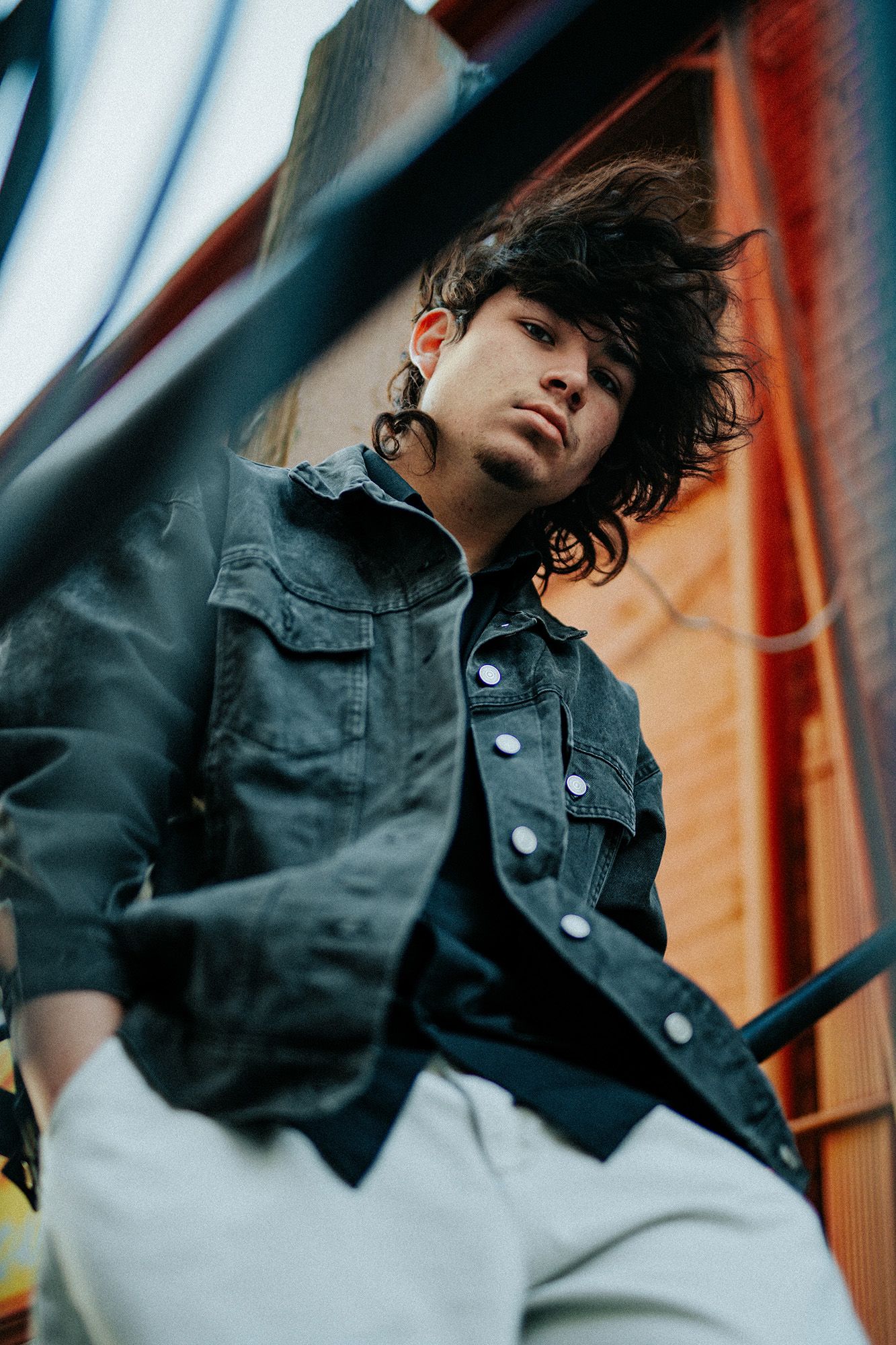 Dramatic low angle portrait showing person in denim jacket against vibrant orange and blue background.