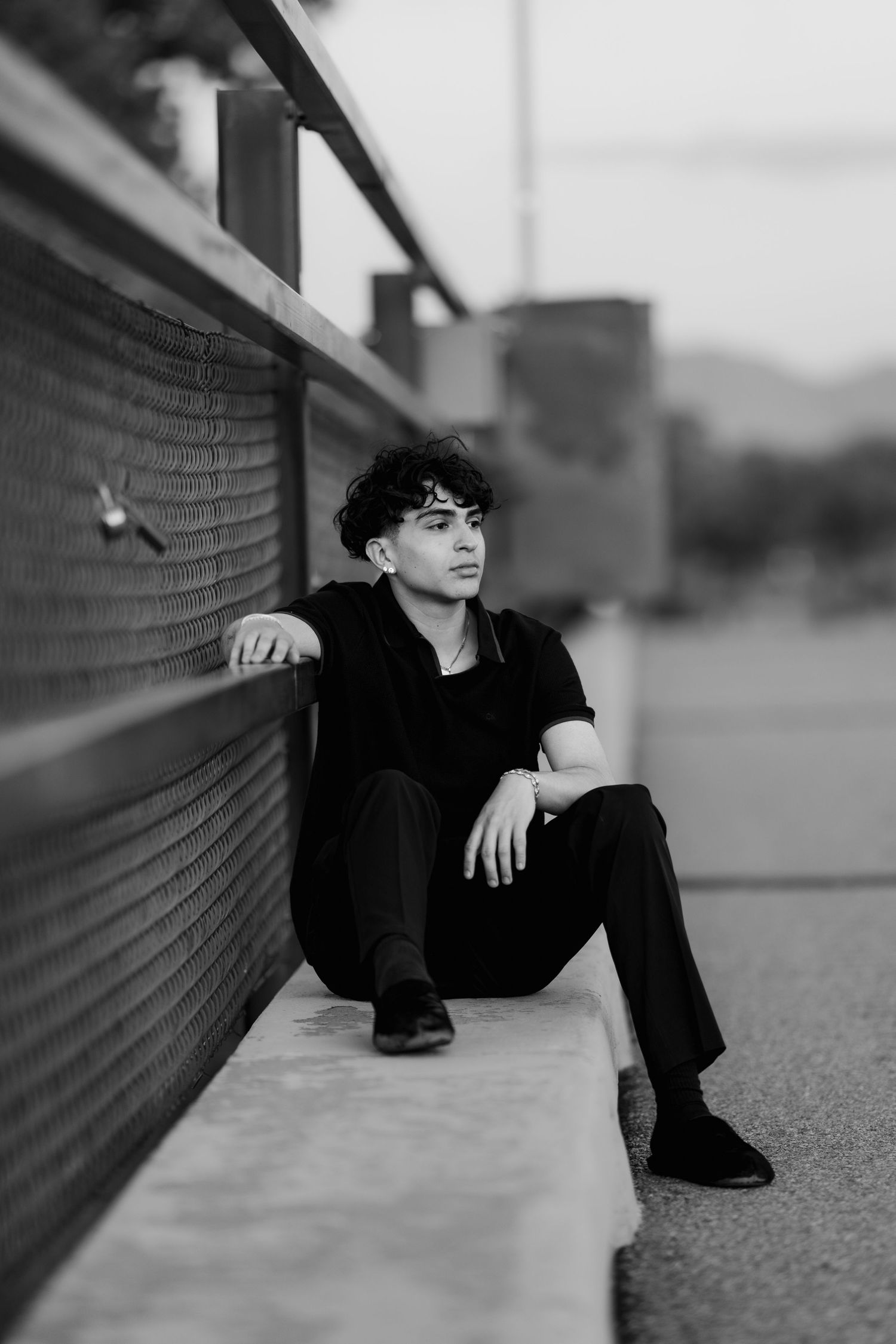 Black and white portrait of someone sitting casually against a wall in dark clothing during a moody outdoor photo session.