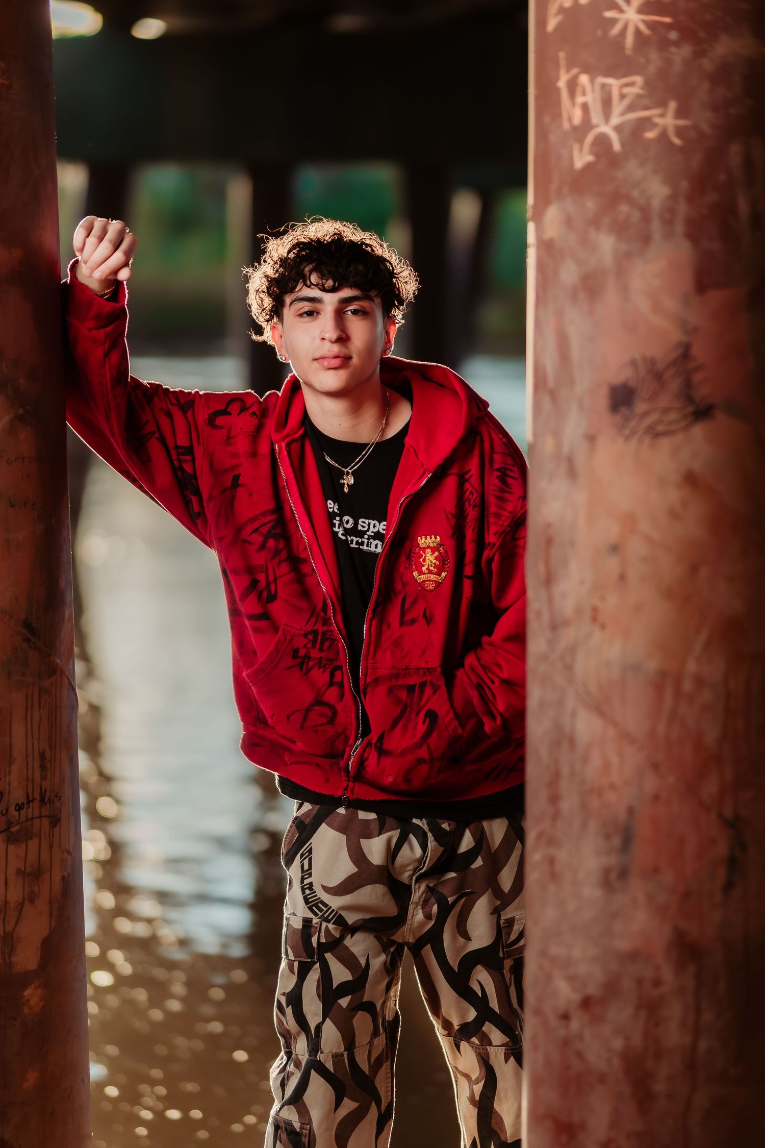 Fashion pose under urban structure wearing red jacket and camo pants.