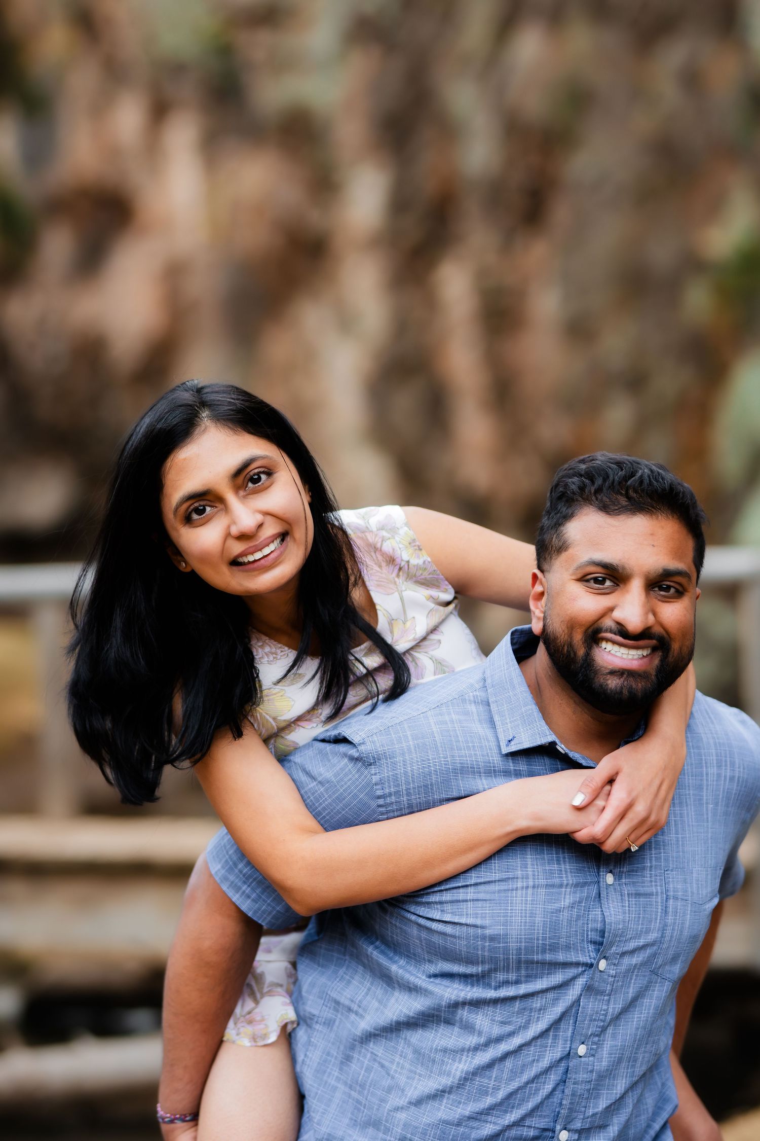 Couple shares playful embrace outdoors with woman hugging from behind in casual portrait session.