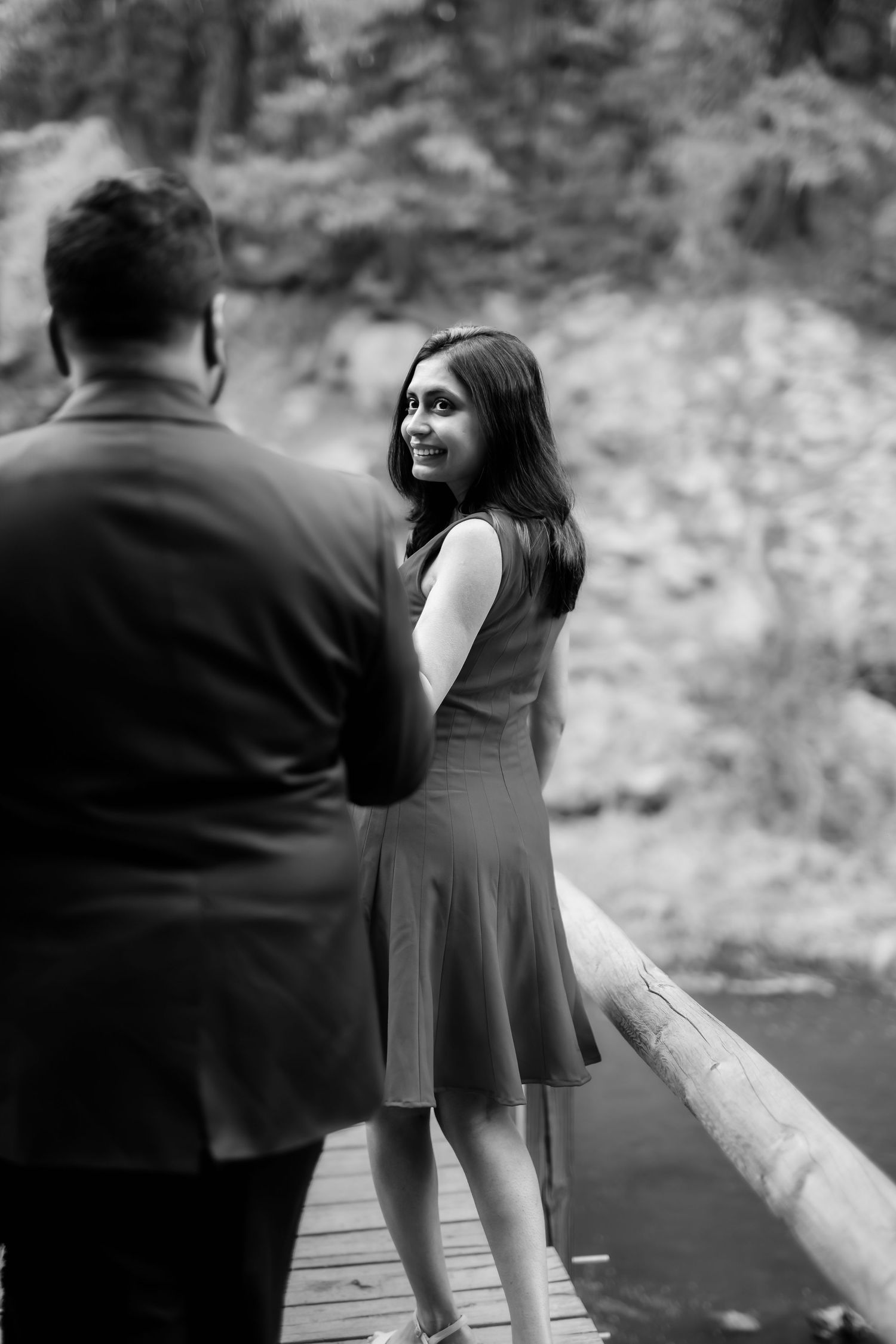 A black and white portrait of a couple sharing a tender moment on a wooden bridge.
