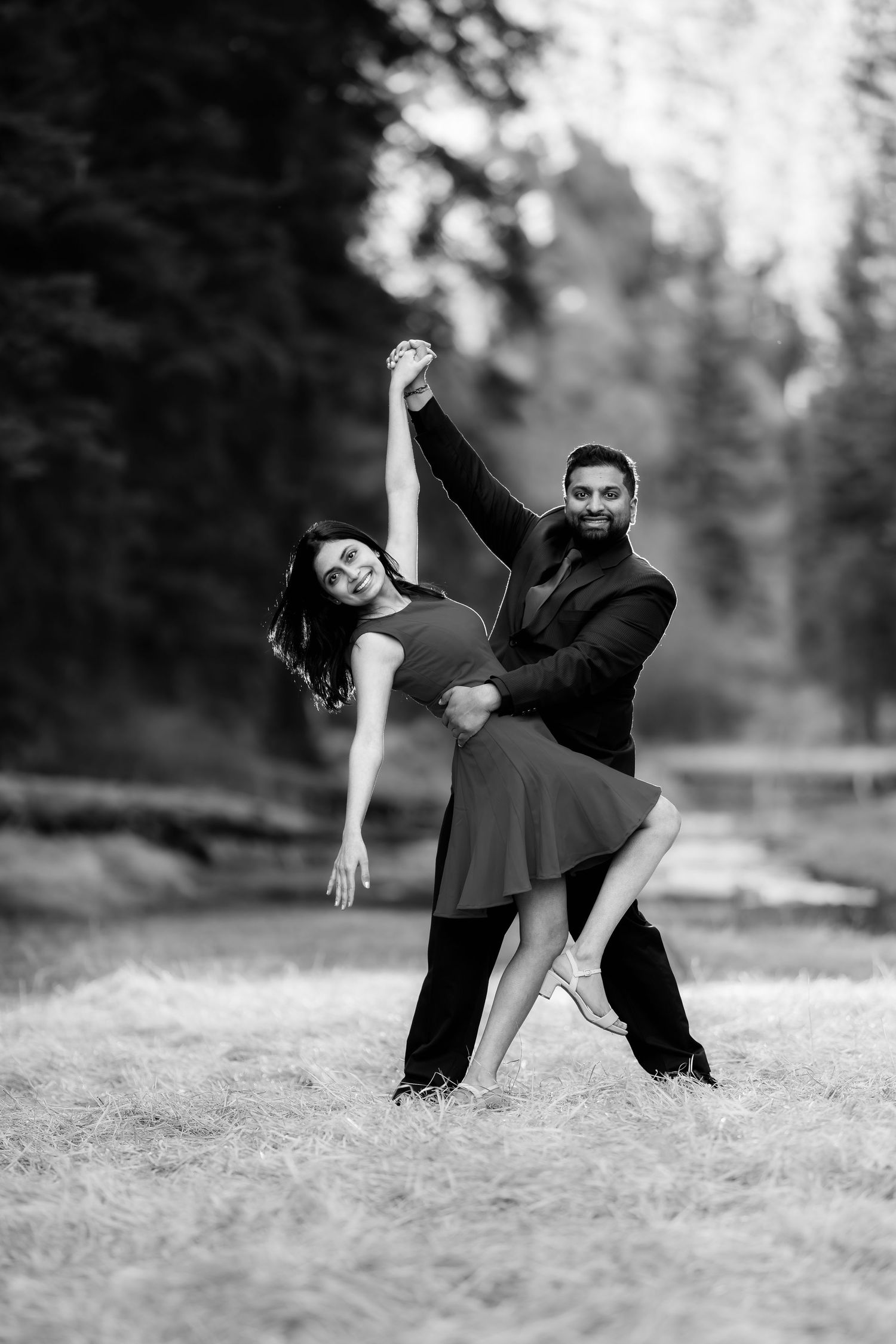 A romantic couple performs an elegant dance pose outdoors in black and white photography.