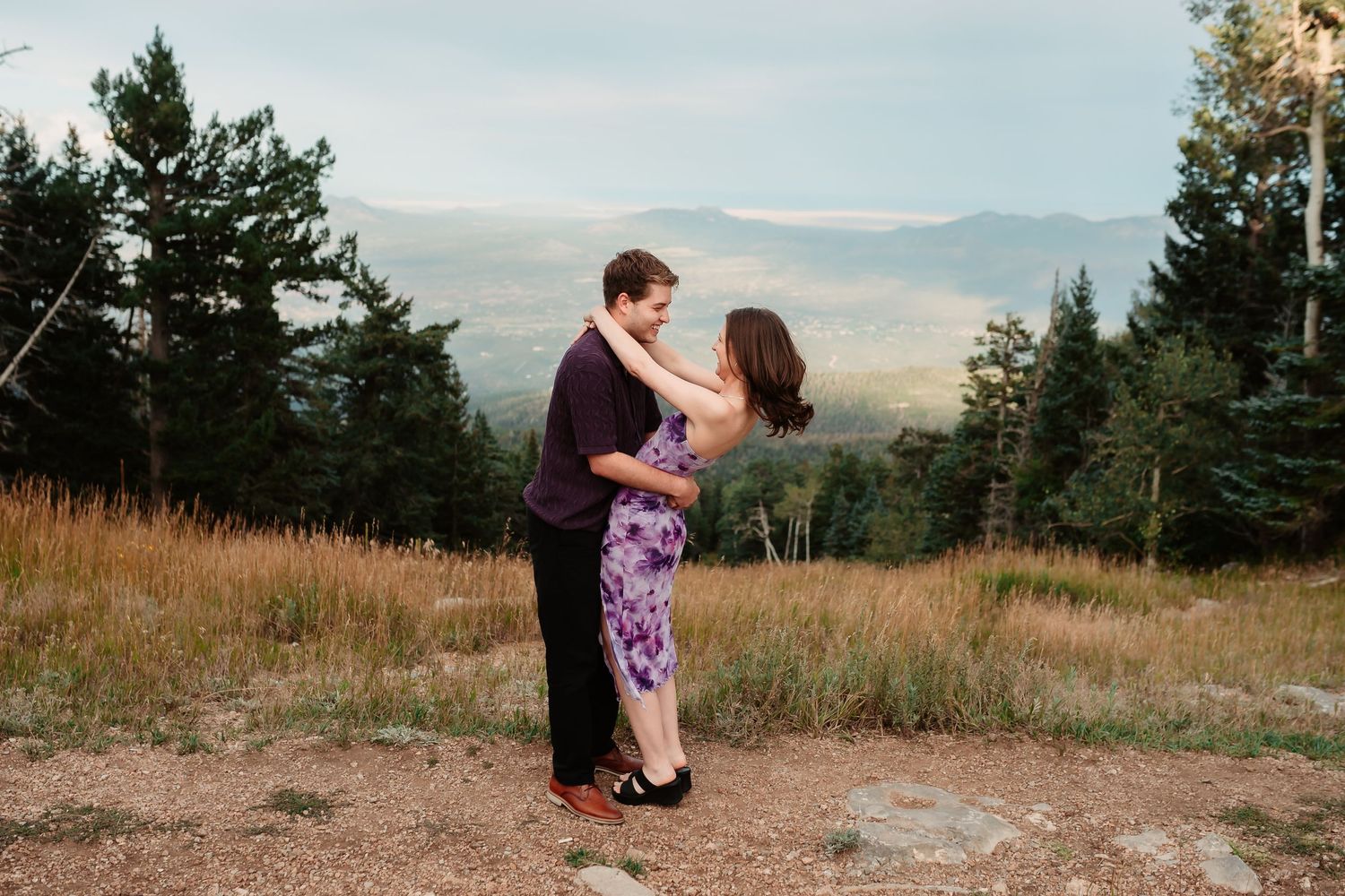 A couple sharing playful moments on a rocky mountain trail.