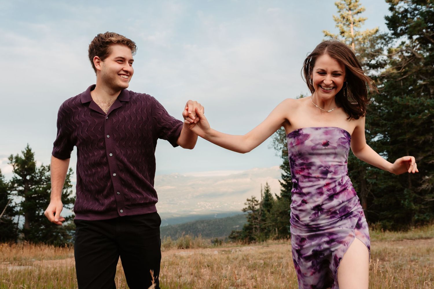 Couple dances joyfully in a mountainside meadow with scenic views.