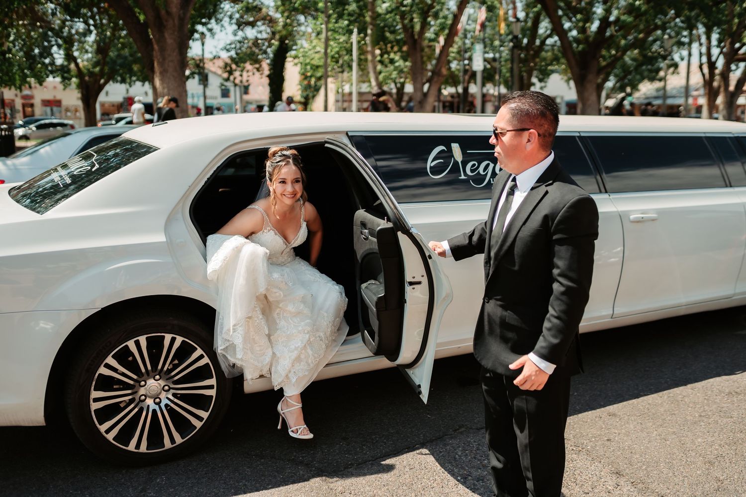 Wedding party gets into a sleek white limousine outside on a sunny day.