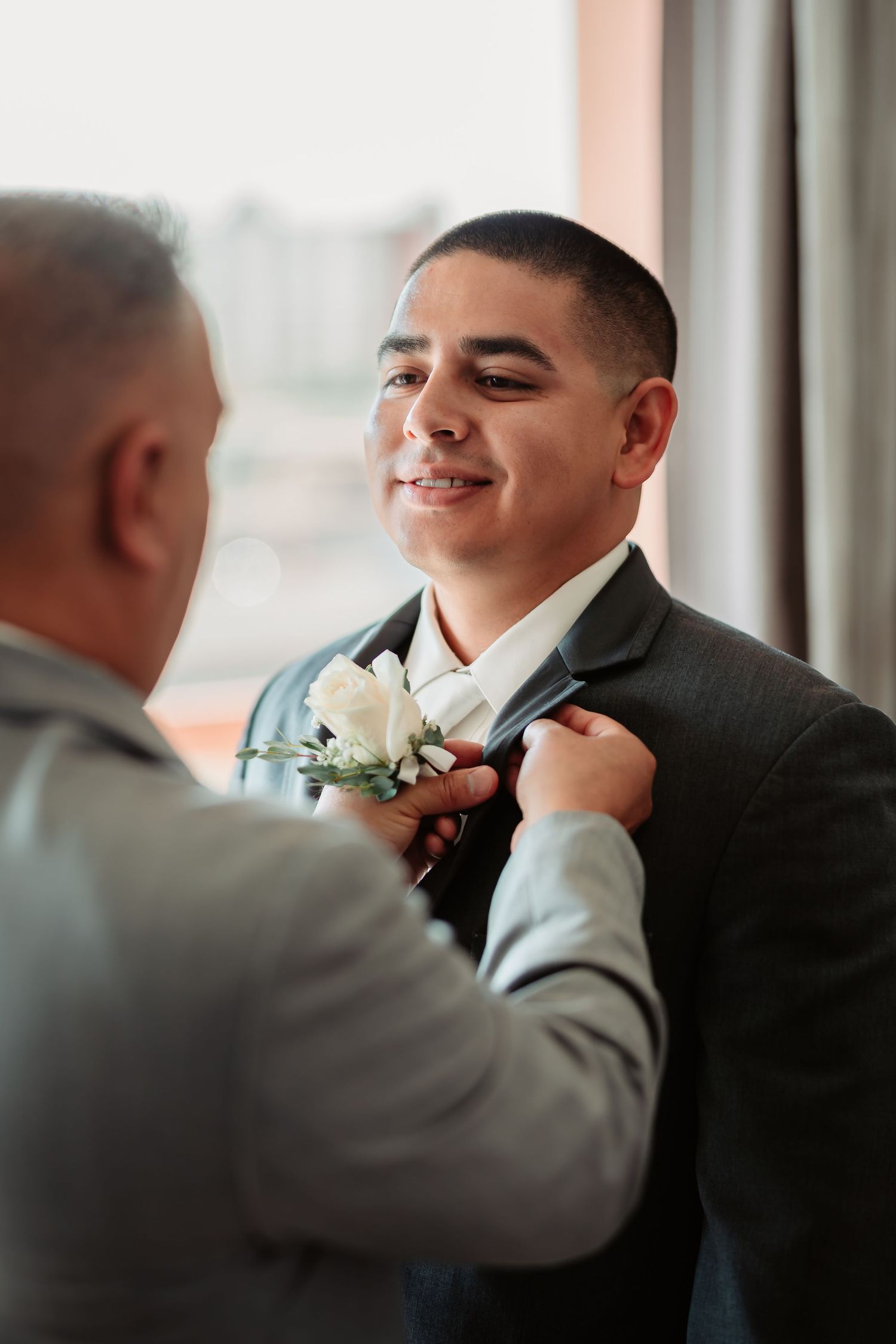 A white boutonniere being adjusted on a dark suit jacket.