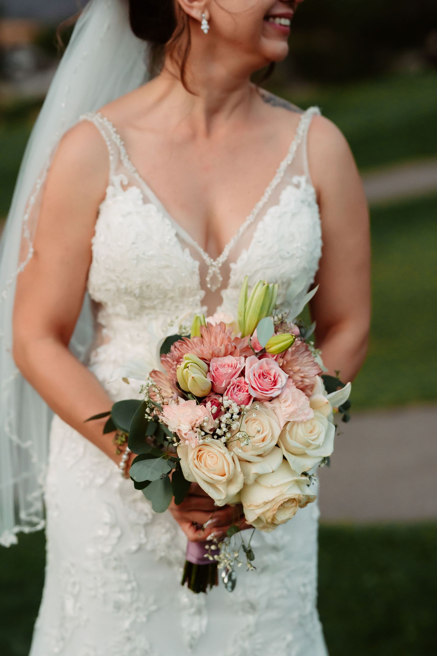 Elegant bridal bouquet with blush roses and mixed flowers against a white lace dress.