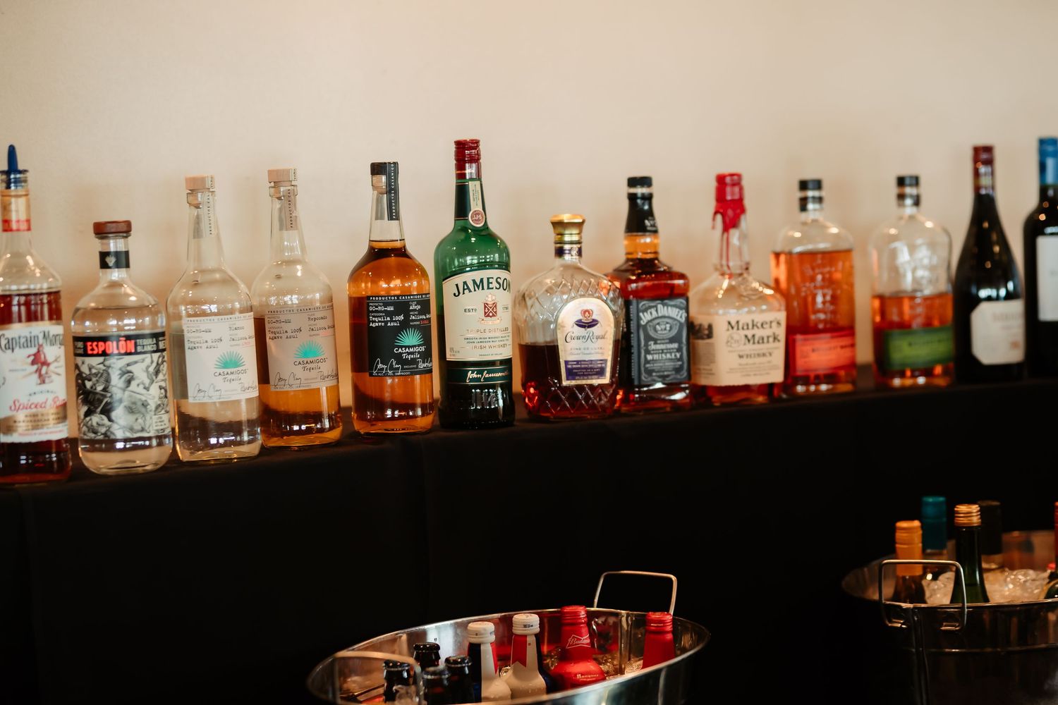 Long shelf display of various liquor and spirit bottles backlit against a dark background.