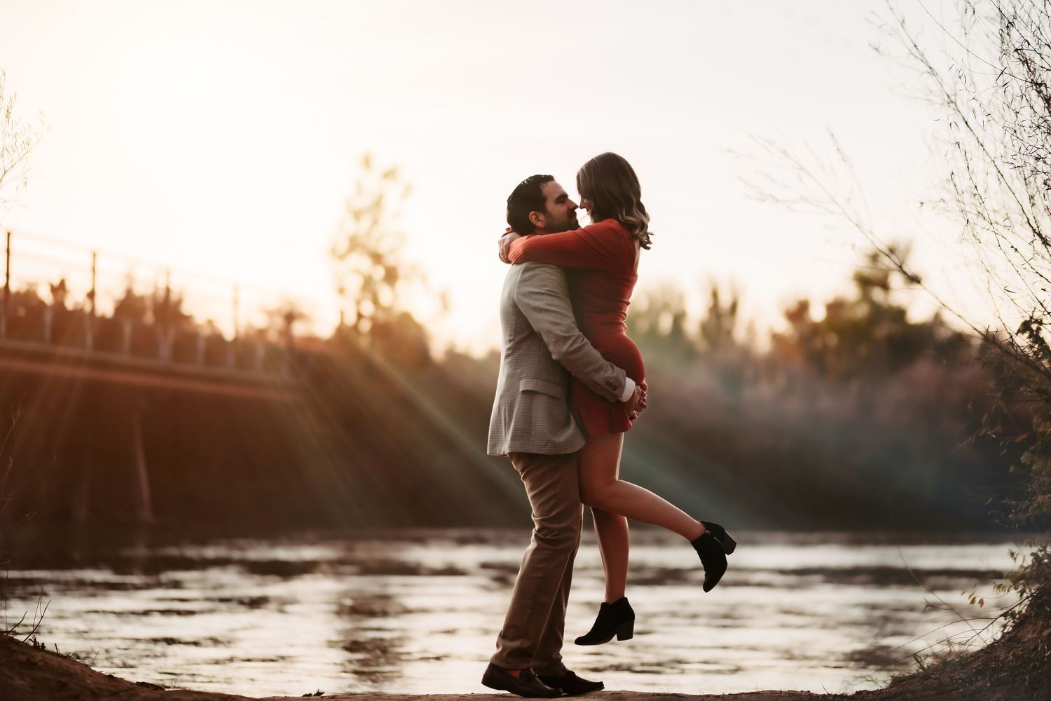 A couple embraces during sunset by a lake creating a romantic silhouette against the golden sky.
