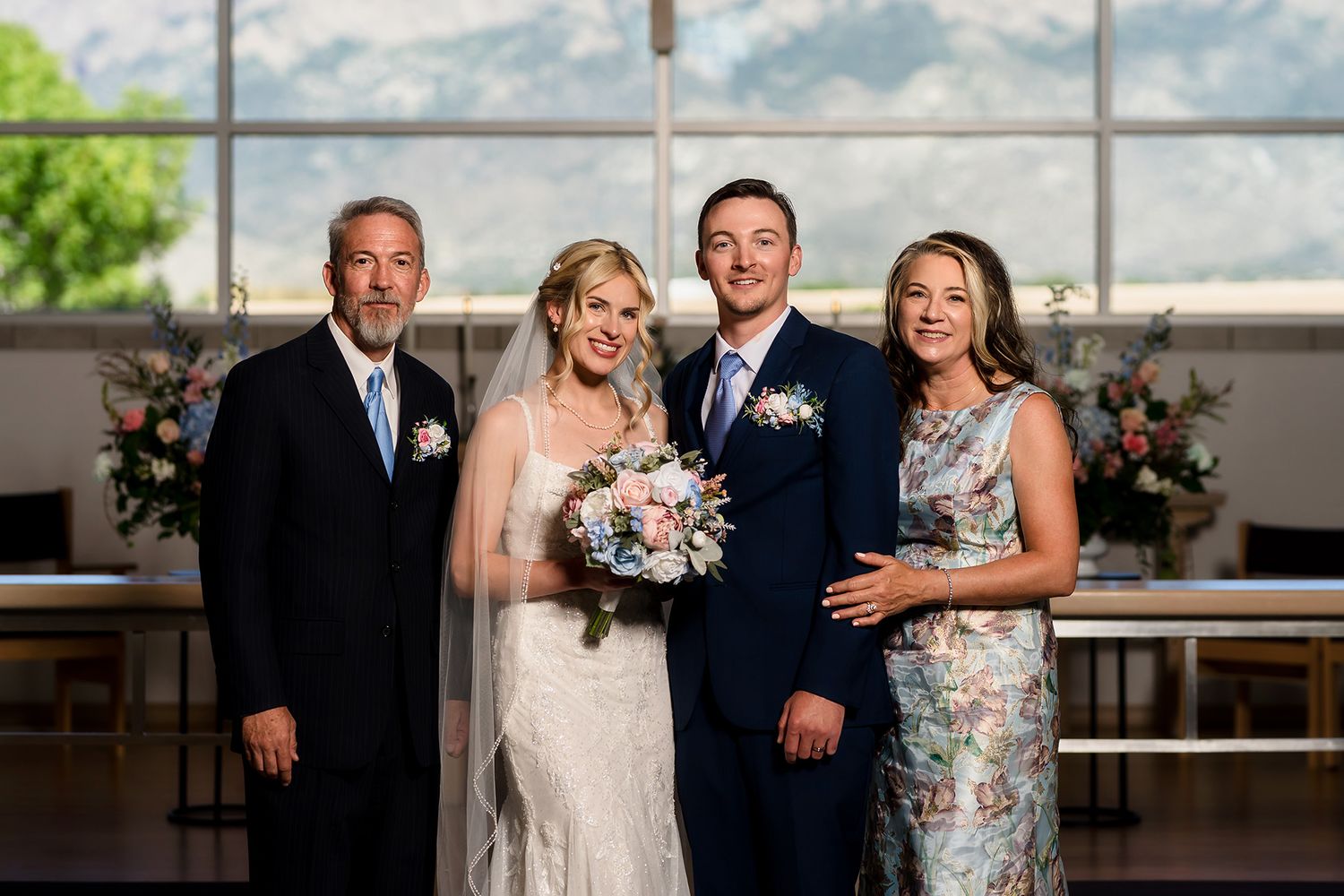 Wedding portrait of bride and groom with two family members in elegant venue with mountain views.