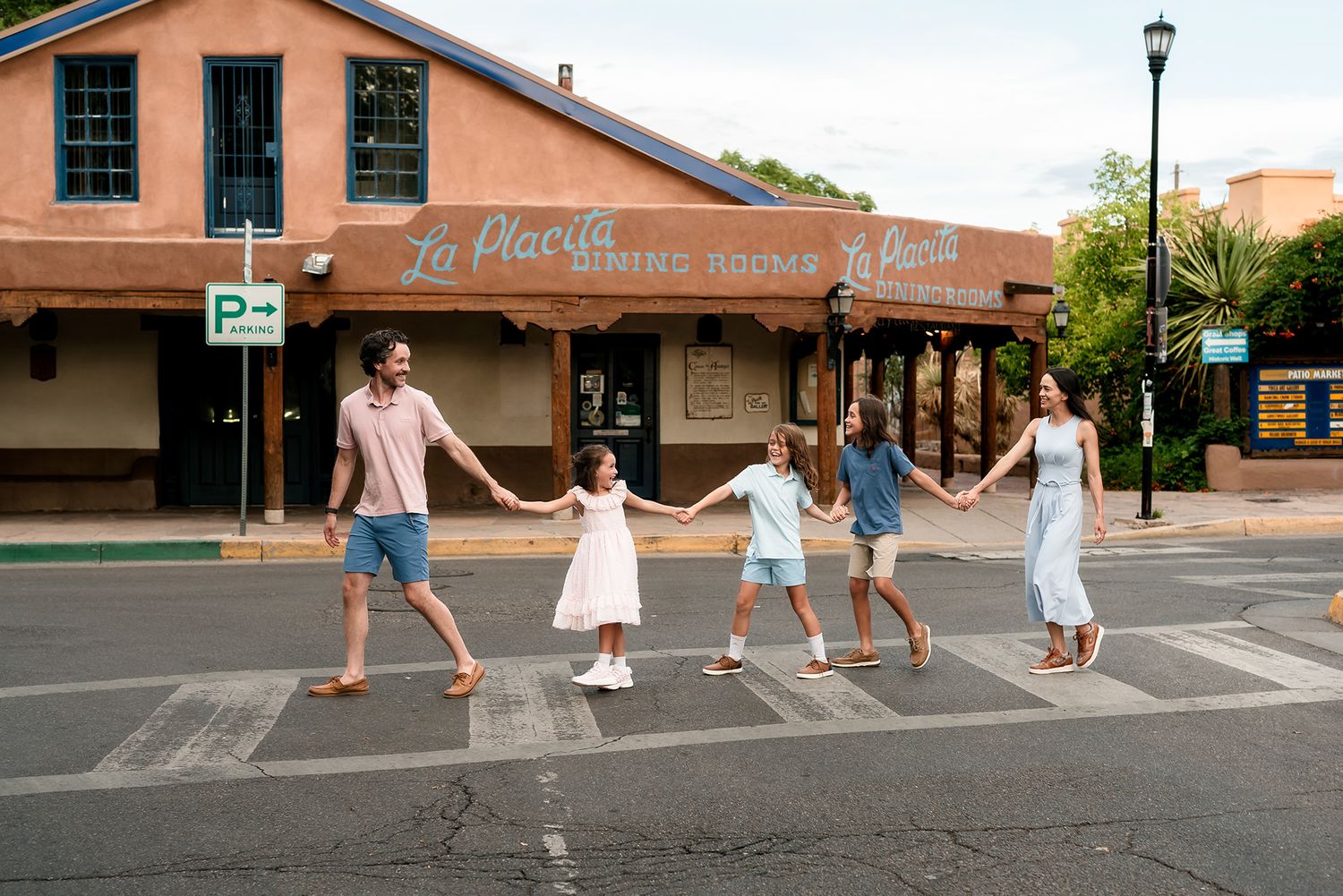 Family of six holding hands crossing a zebra crossing in front of La Placita restaurant on a sunny day.