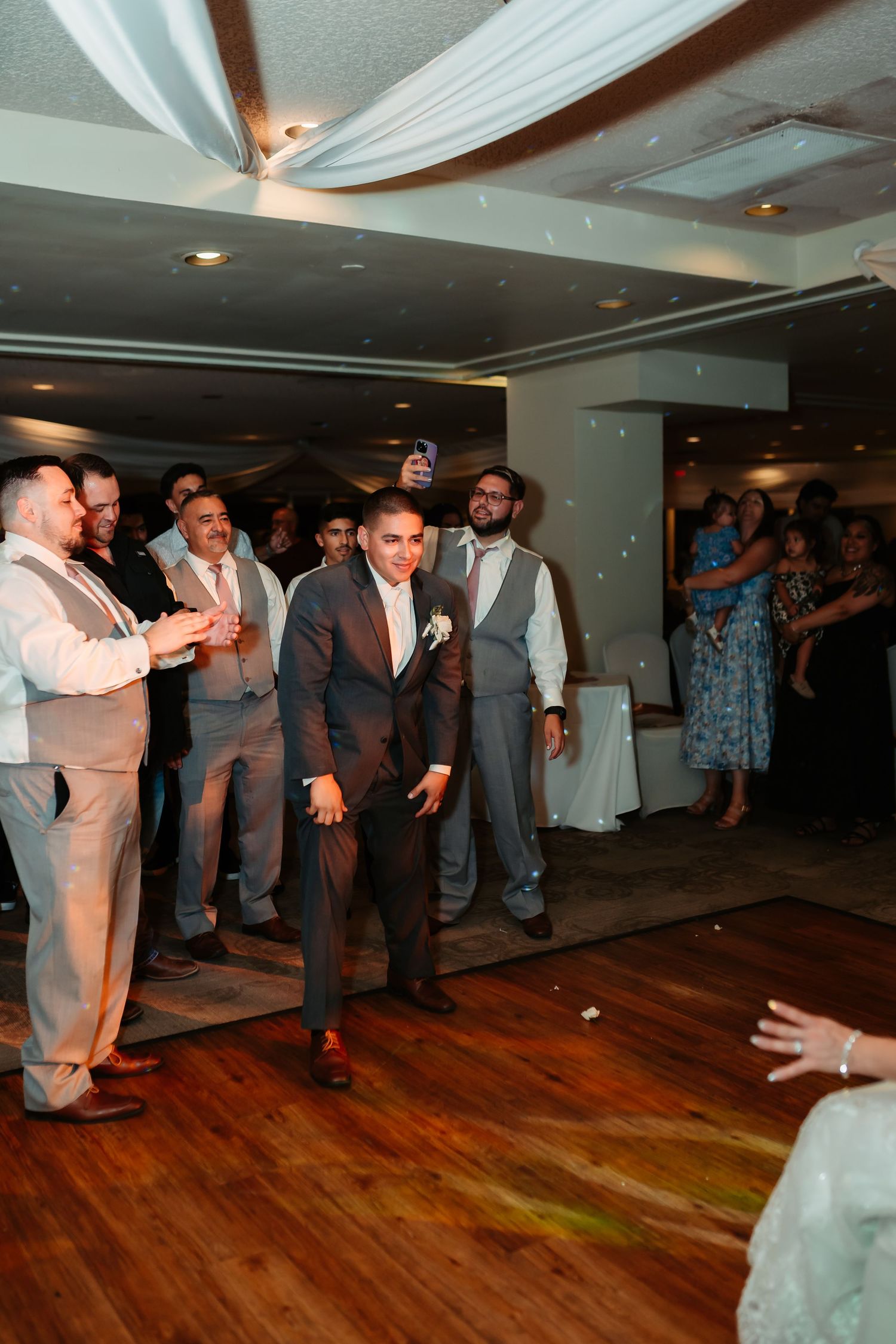 Guests at a wedding reception cheer on dancers enjoying themselves on a wooden dance floor.