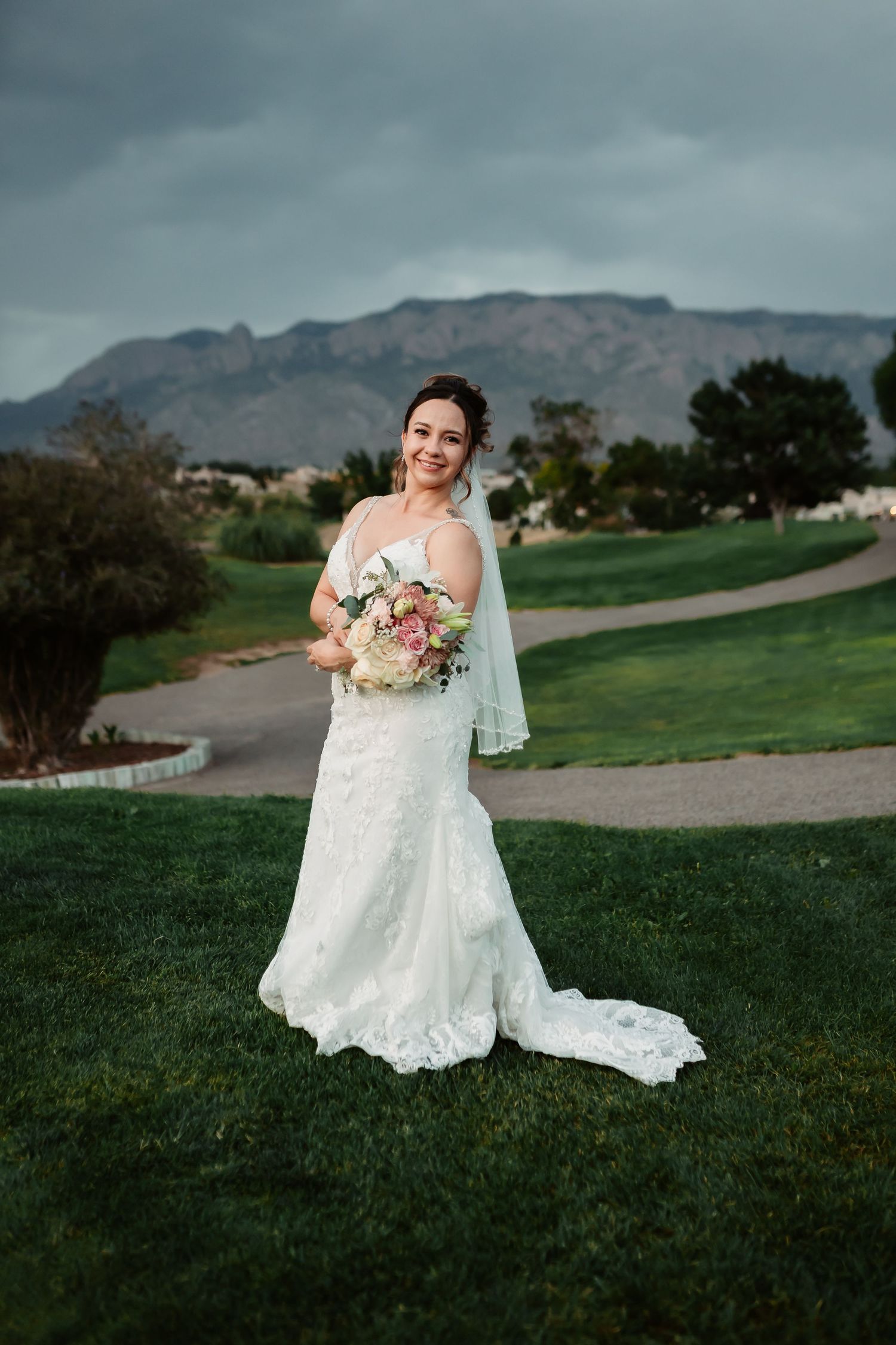 Bride in elegant lace gown poses against mountainous landscape with scenic backdrop.