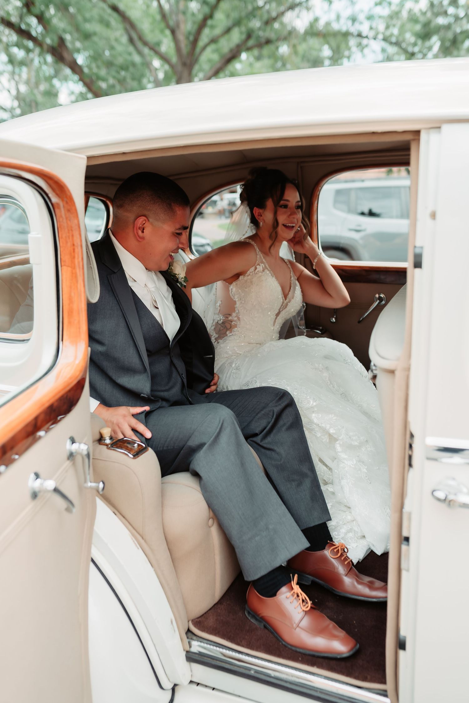 Newlyweds entering a classic vintage car with beige interior on their wedding day.