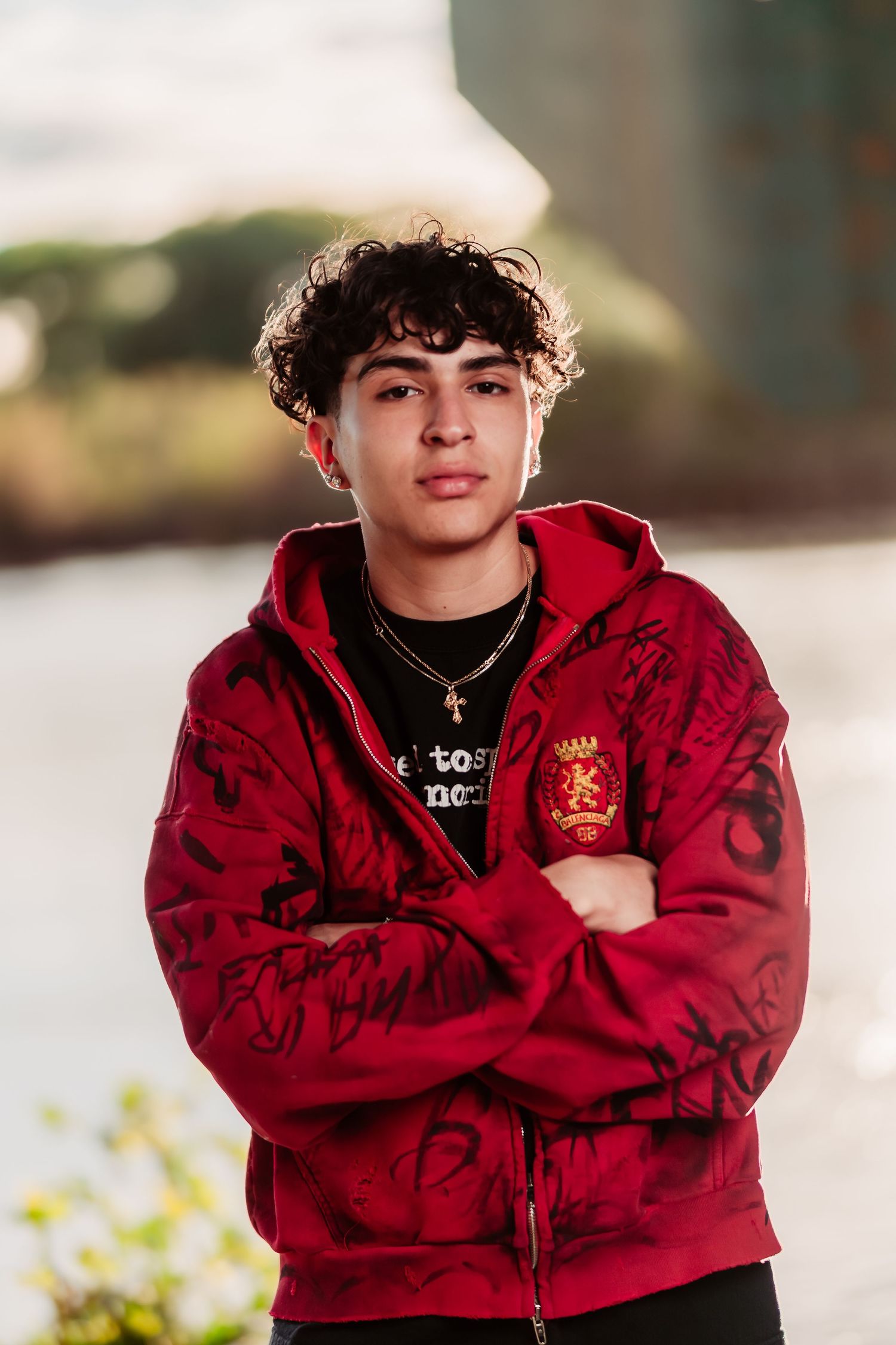 Young person wearing a red branded hoodie with curly hair poses outdoors.