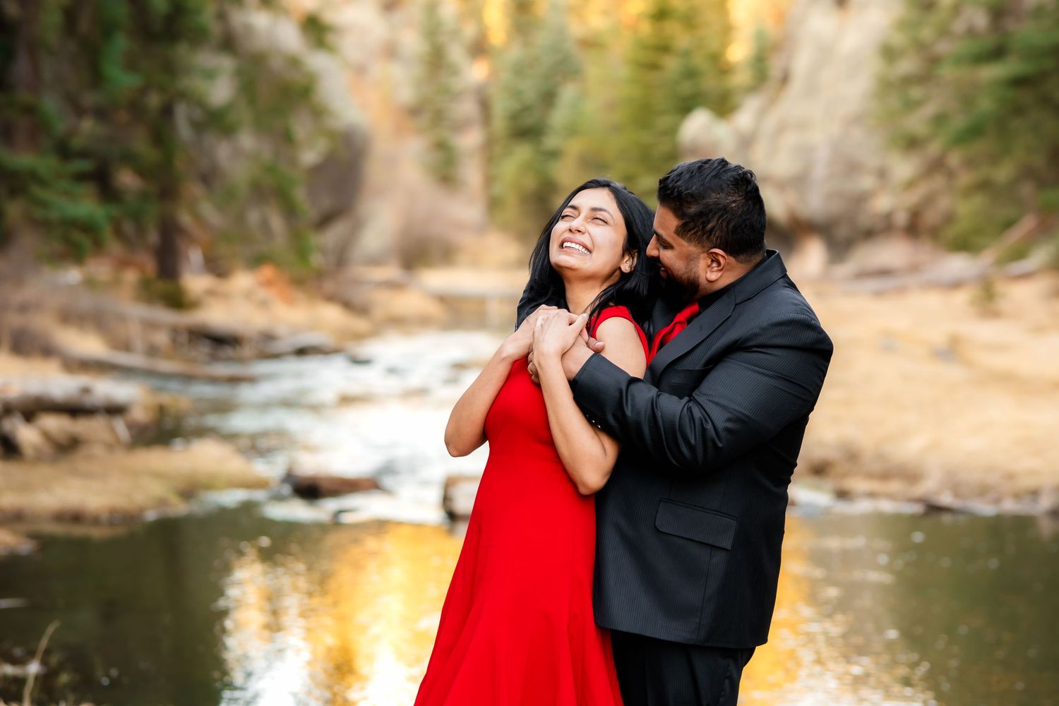 Couple shares intimate moment beside reflective mountain stream during golden hour.