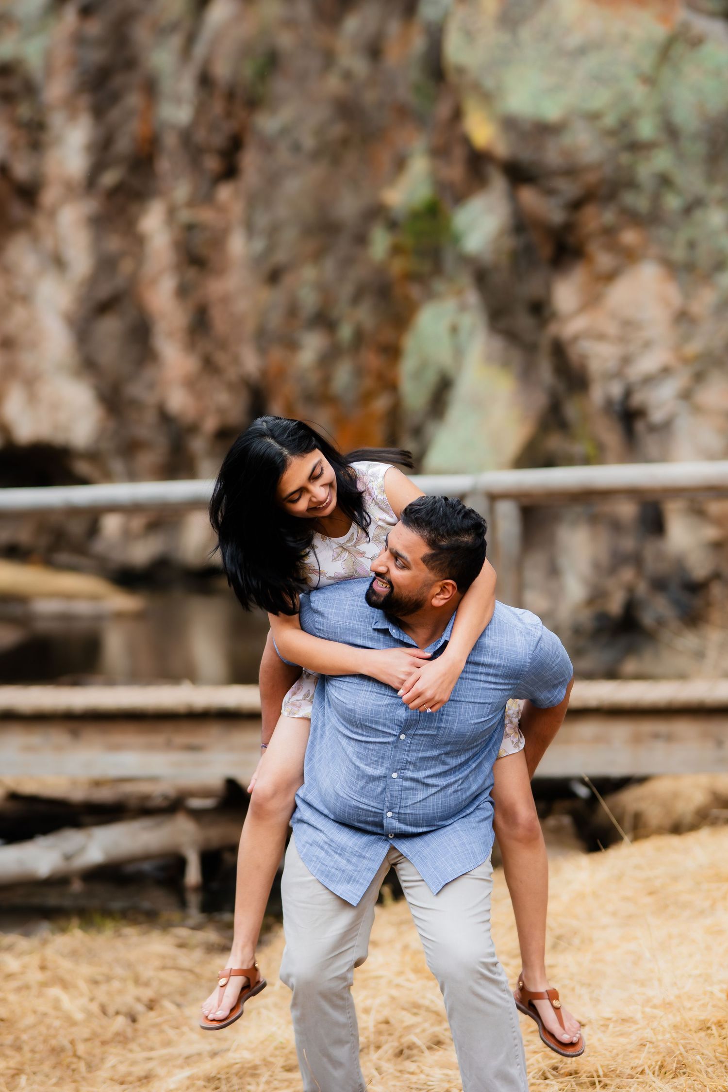 A playful couple shares a piggyback ride moment outdoors against rocky cliffs.