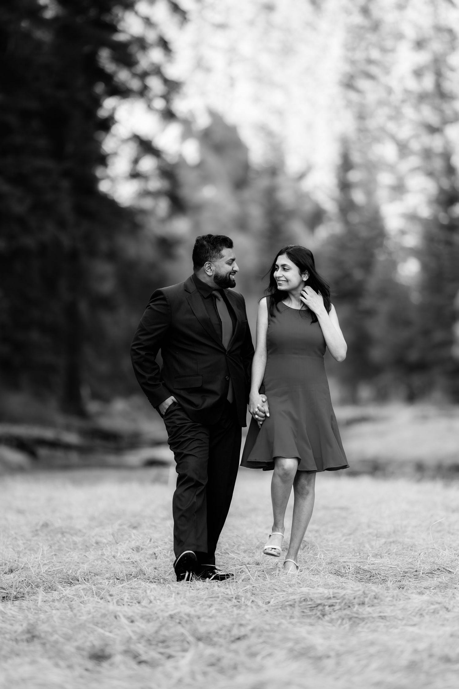 A couple in formal attire stands together in a black and white forest setting.