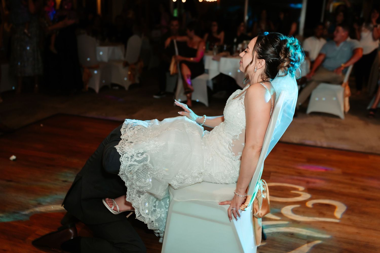 A dramatic wedding dance dip on a wooden dance floor during a reception with colored lighting.
