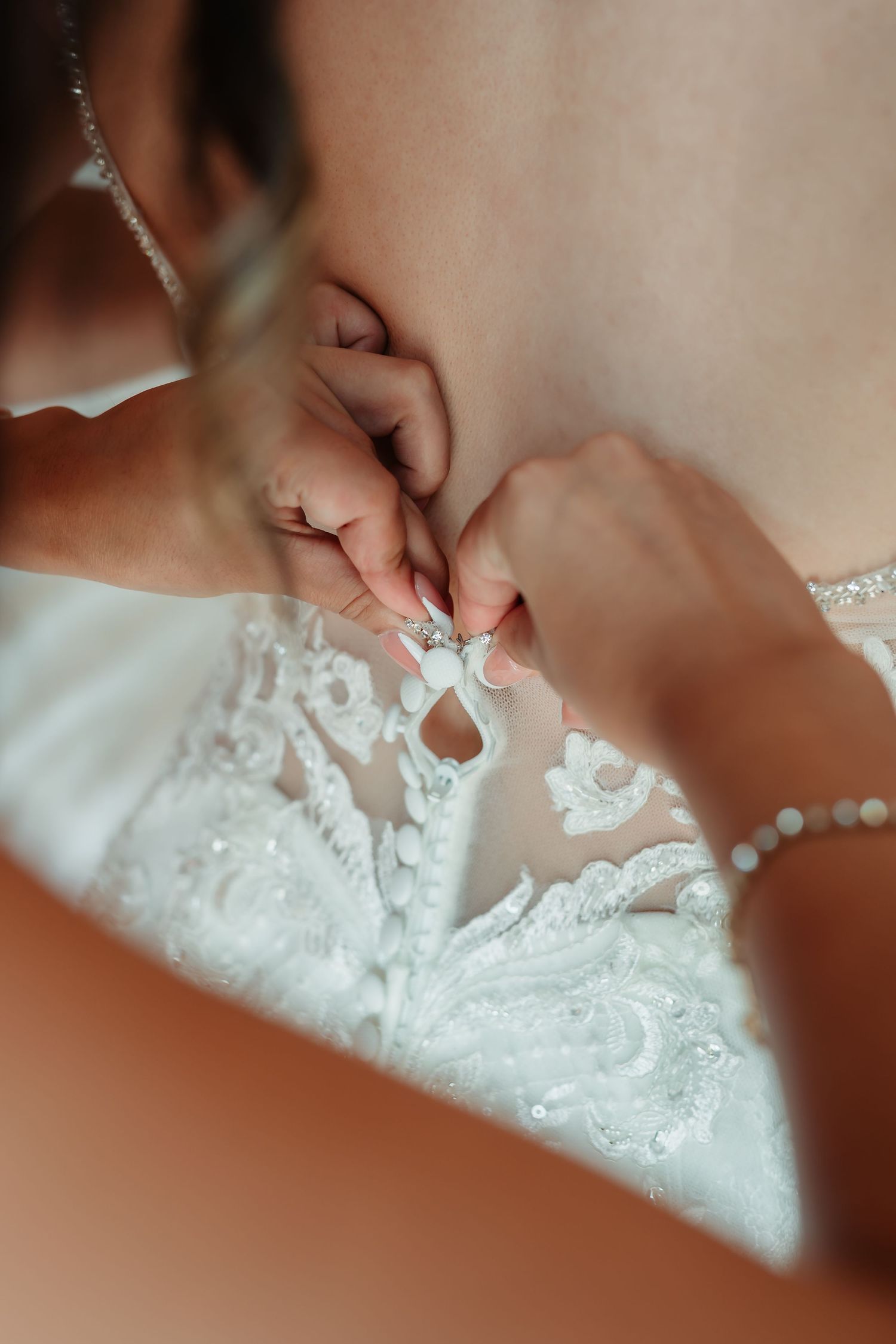 Close-up detail of delicate pearl buttons and lace on a white wedding dress.