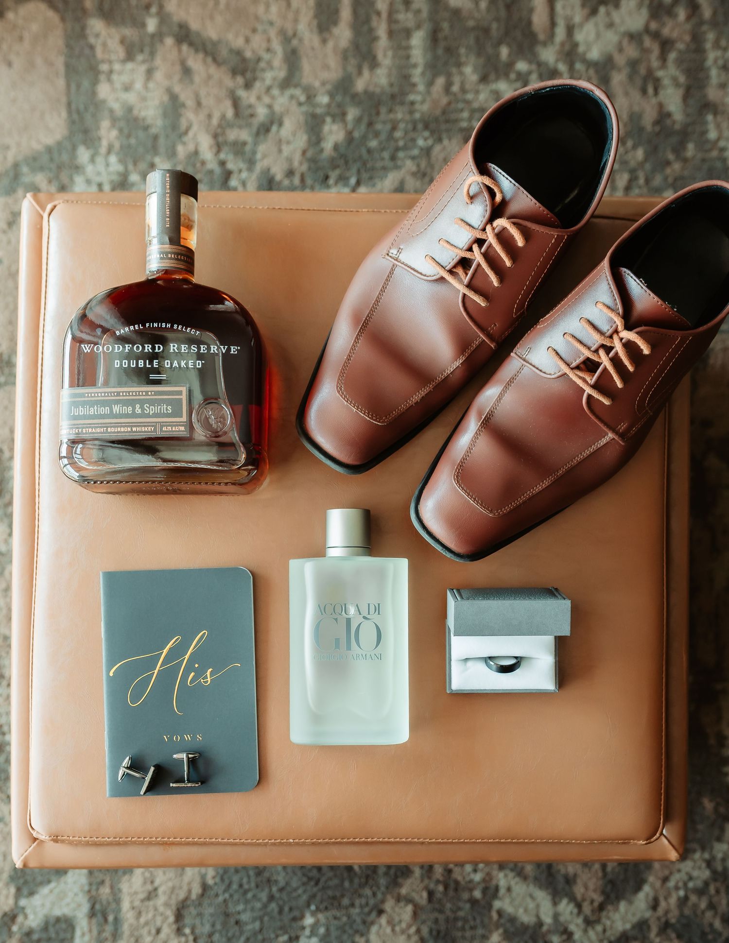 Wedding accessories including brown leather dress shoes, cufflinks, and stationery arranged on a light brown surface.