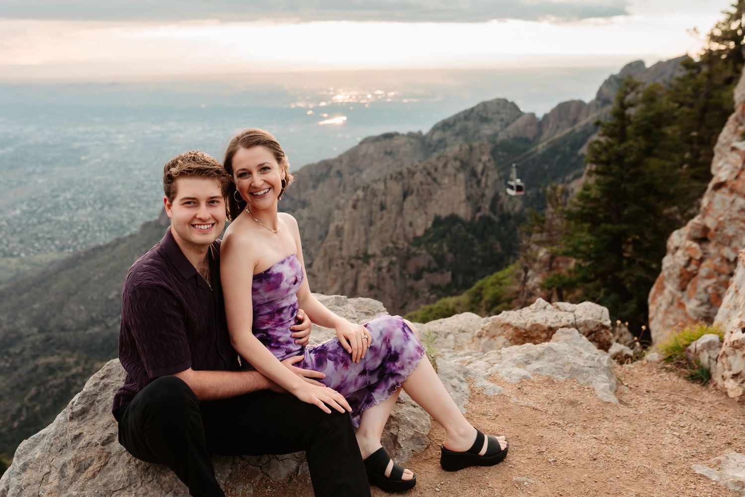 Romantic couple poses together on mountain overlook with expansive valley views and warm evening light.