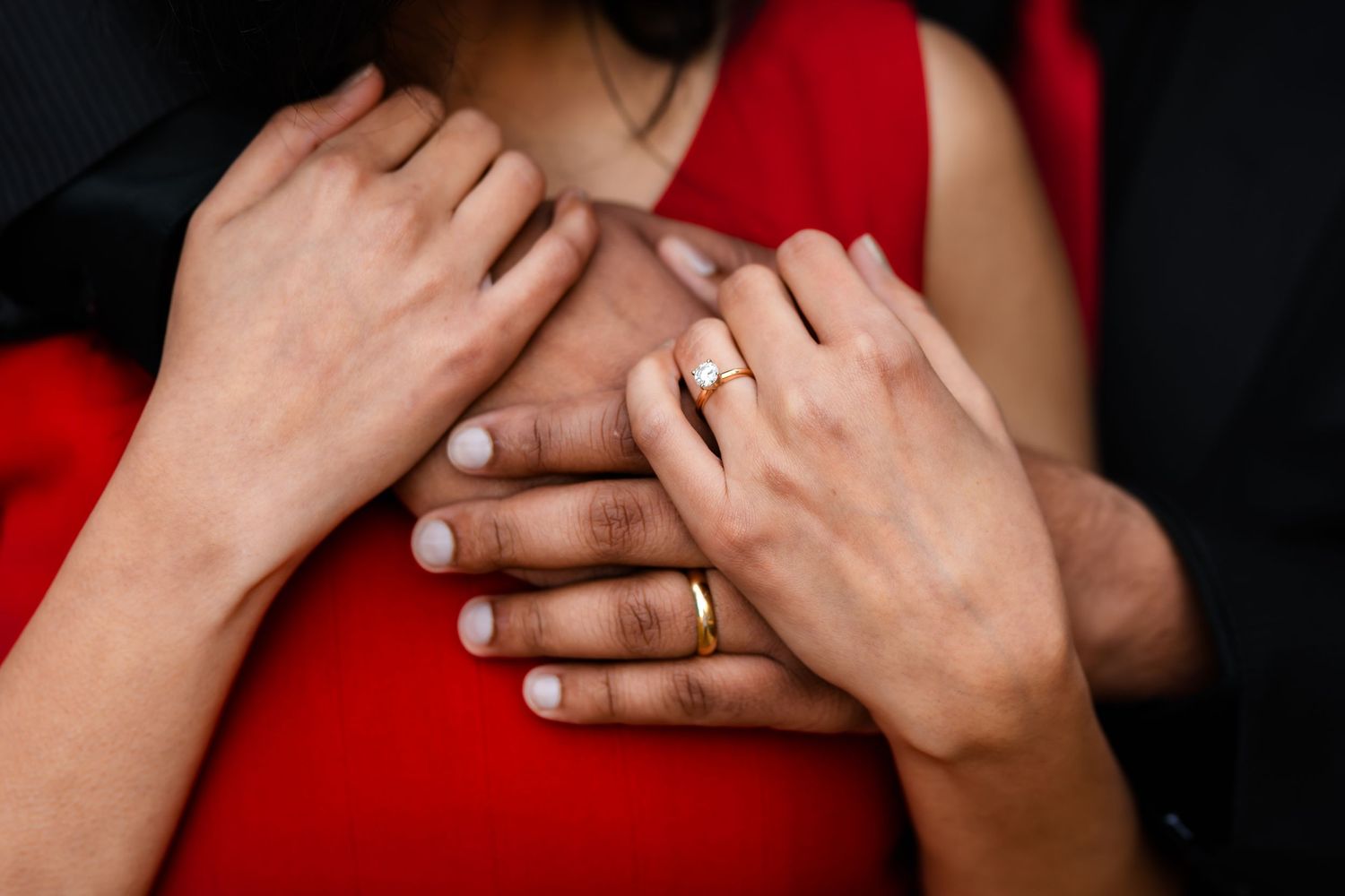 Close-up shot of hands with engagement ring against red dress and black suit.