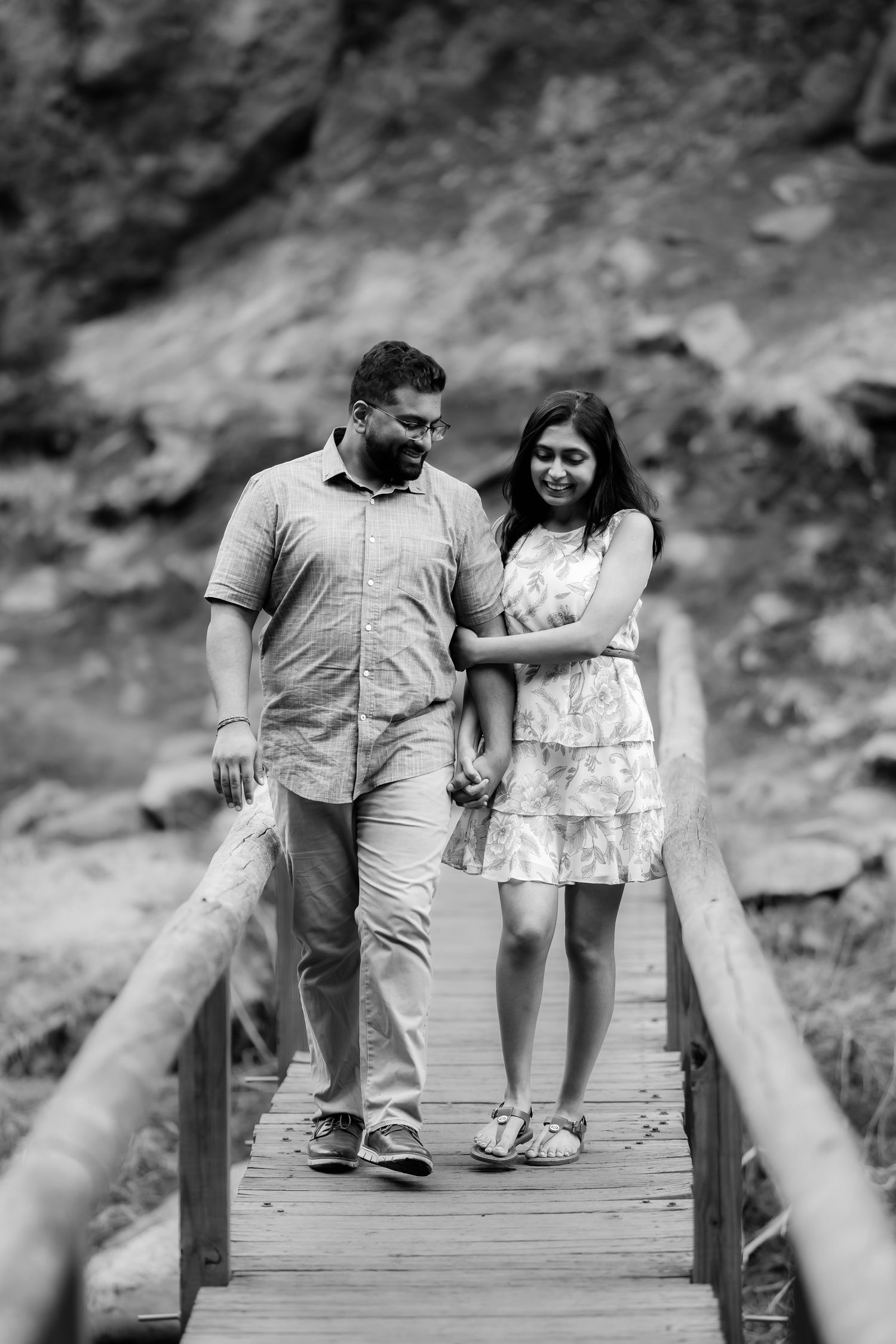 A couple holds hands while walking together on a wooden footbridge in black and white photography.