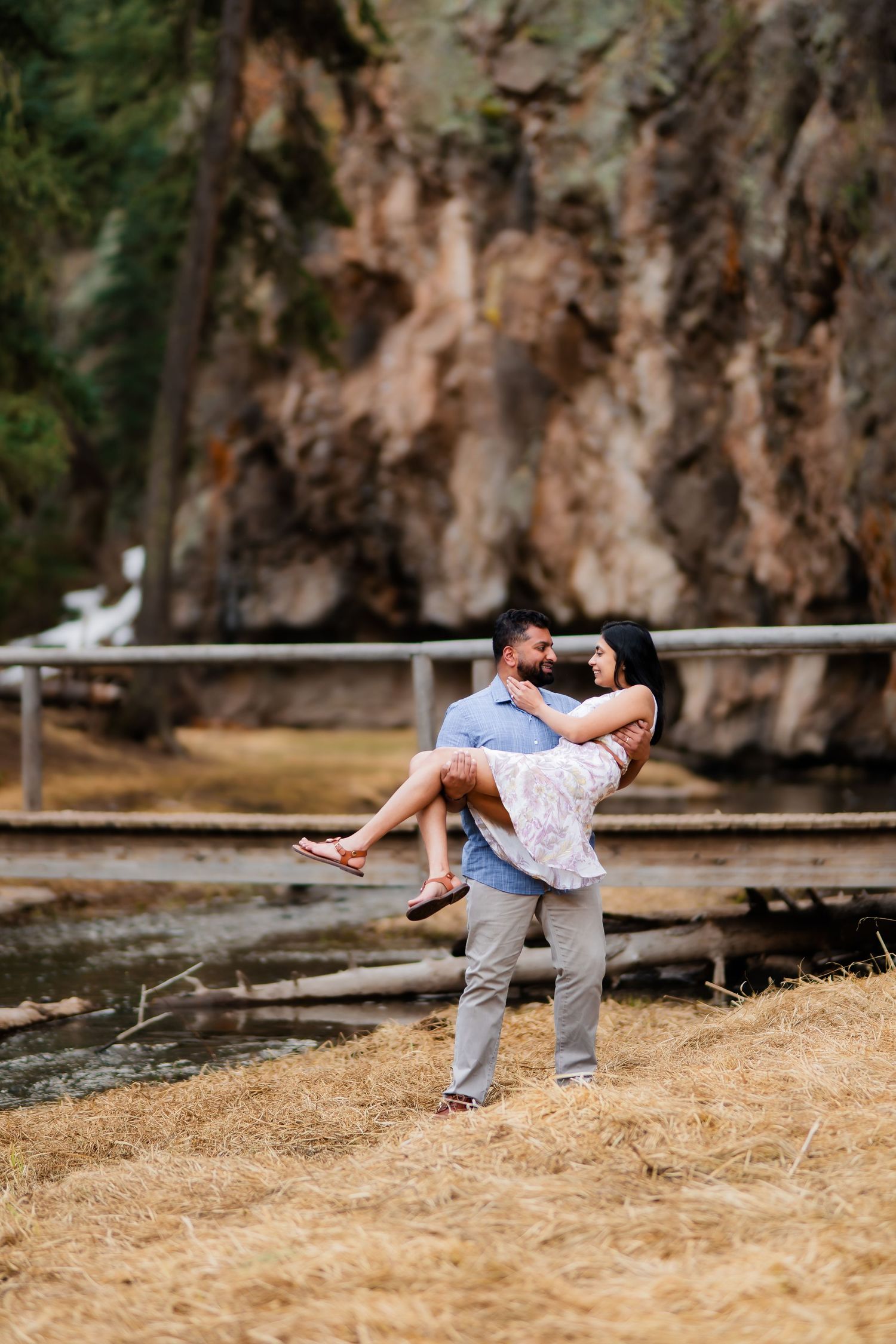 A playful couple shares a joyful moment as he carries her near a scenic mountain stream.