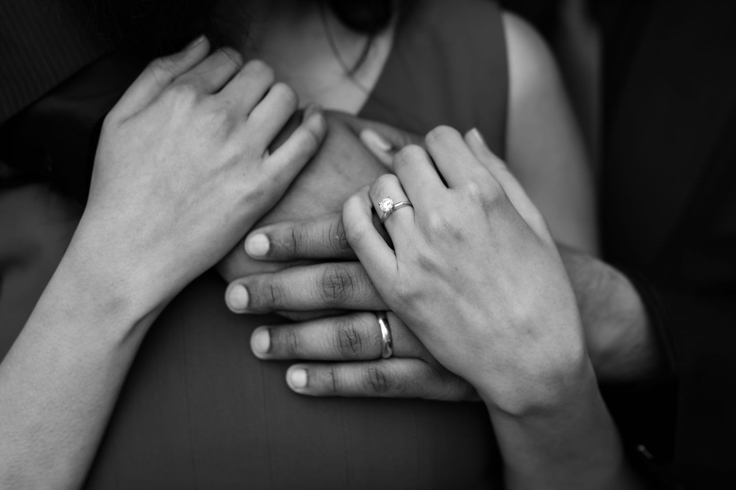 A close-up black and white shot of hands with an engagement ring.